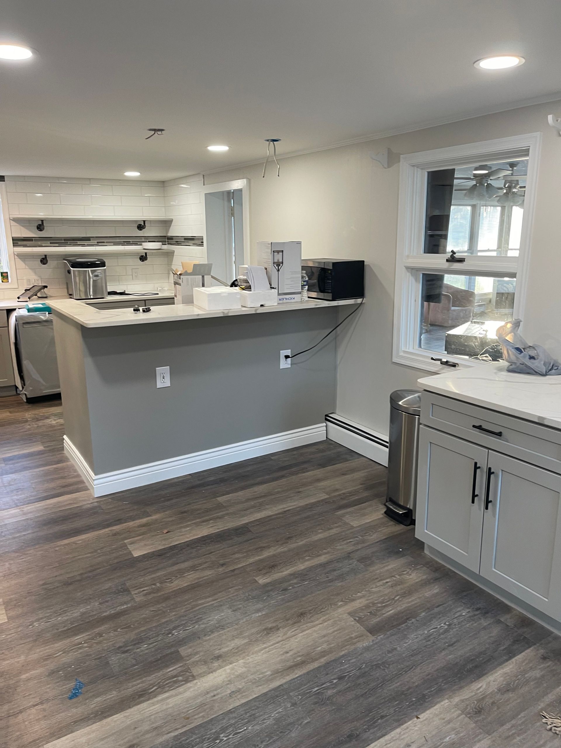 Kitchen renovation: gray island, white cabinets, new wood-look flooring, and window with natural light.