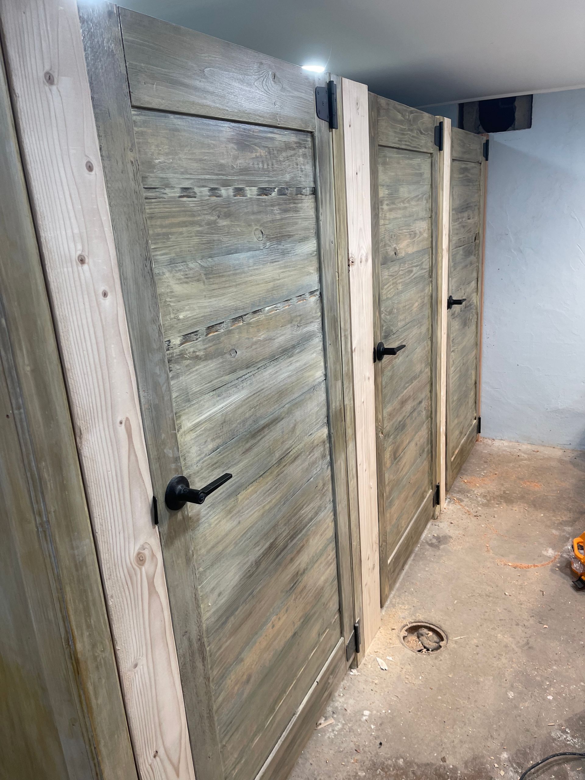 Three weathered wooden doors with black handles and light wood frames.