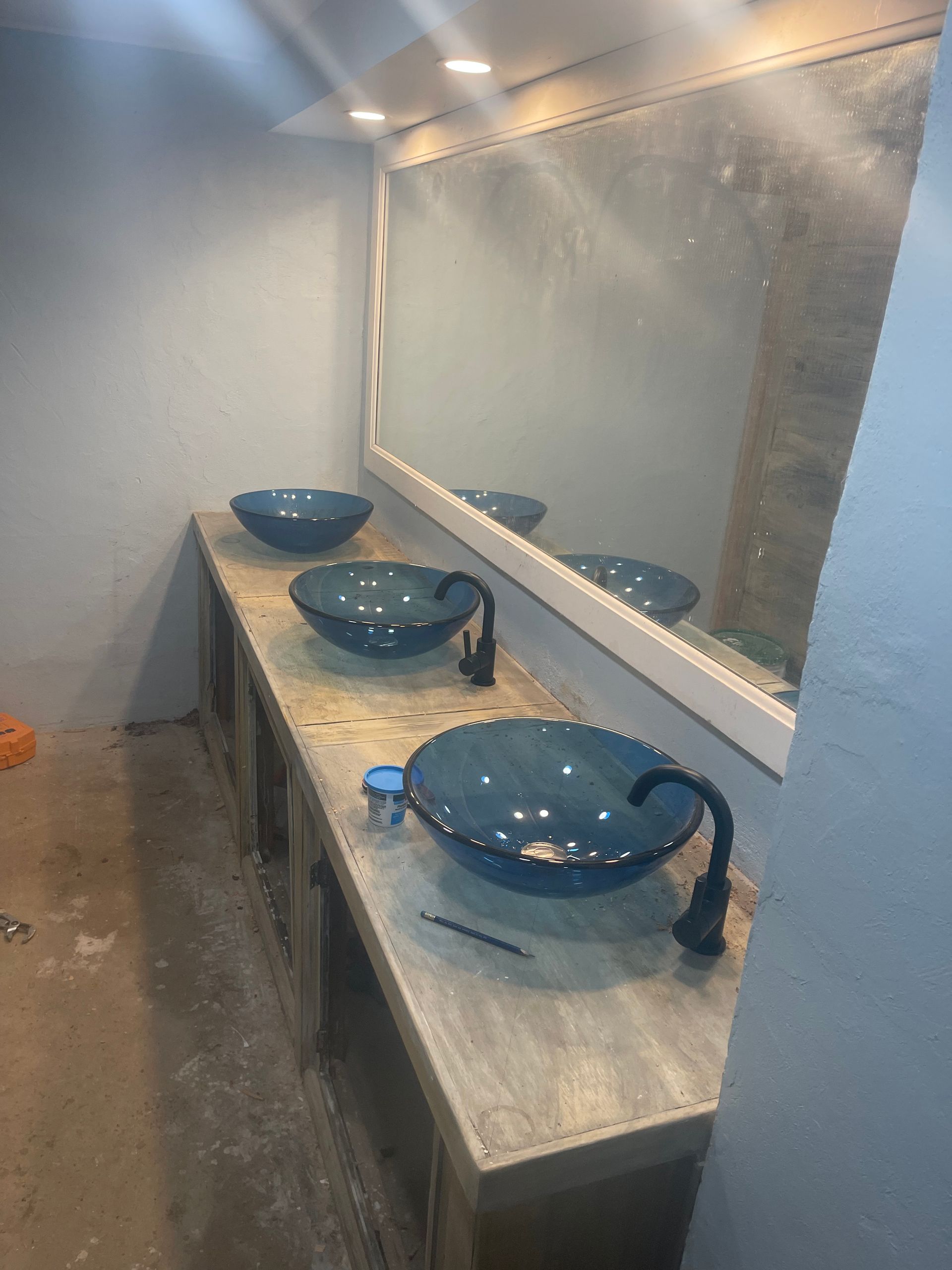 Bathroom with three blue vessel sinks on a wooden vanity, large mirror, and black faucets.
