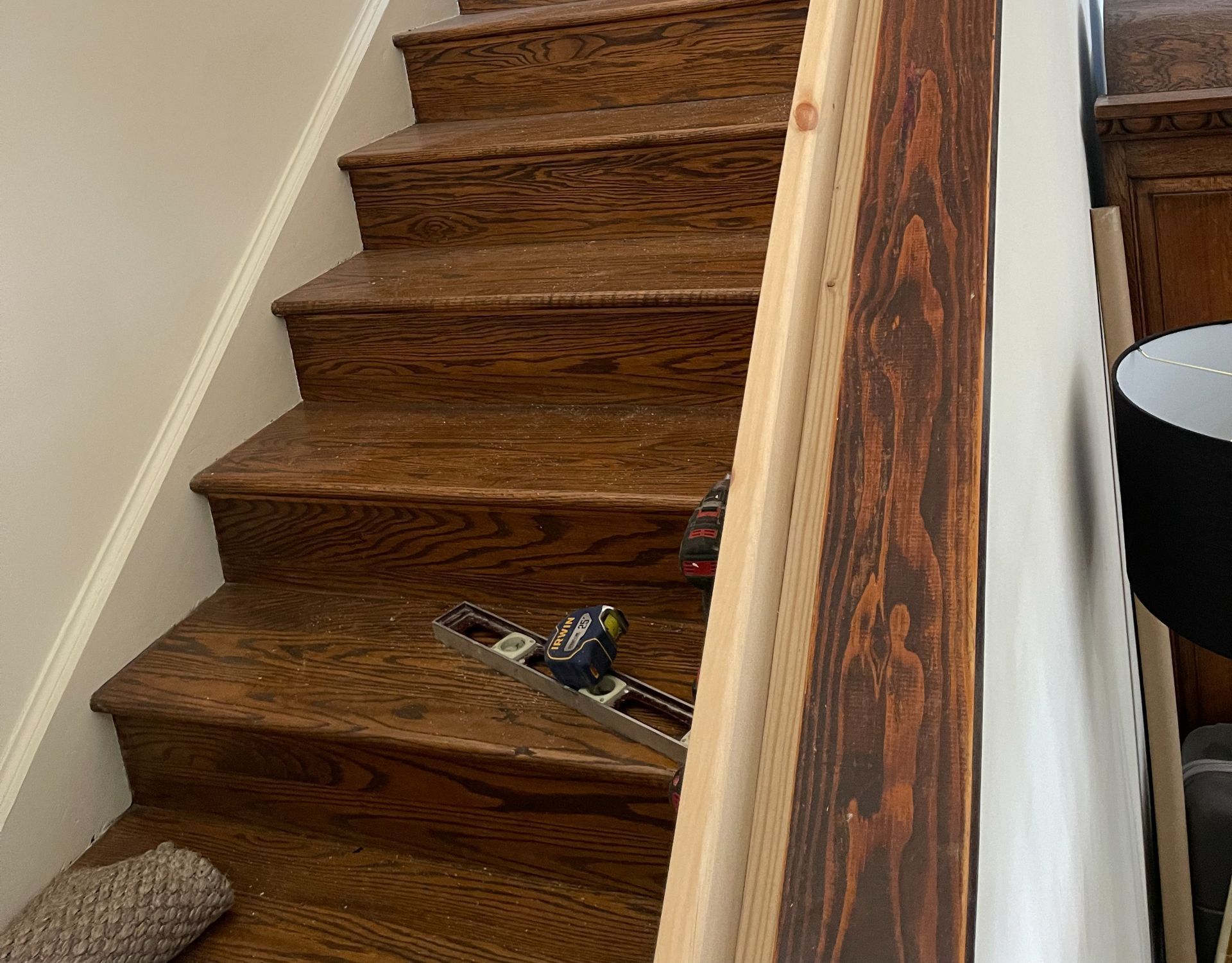 Wooden staircase with handrail, tool, and partial carpet on the steps.