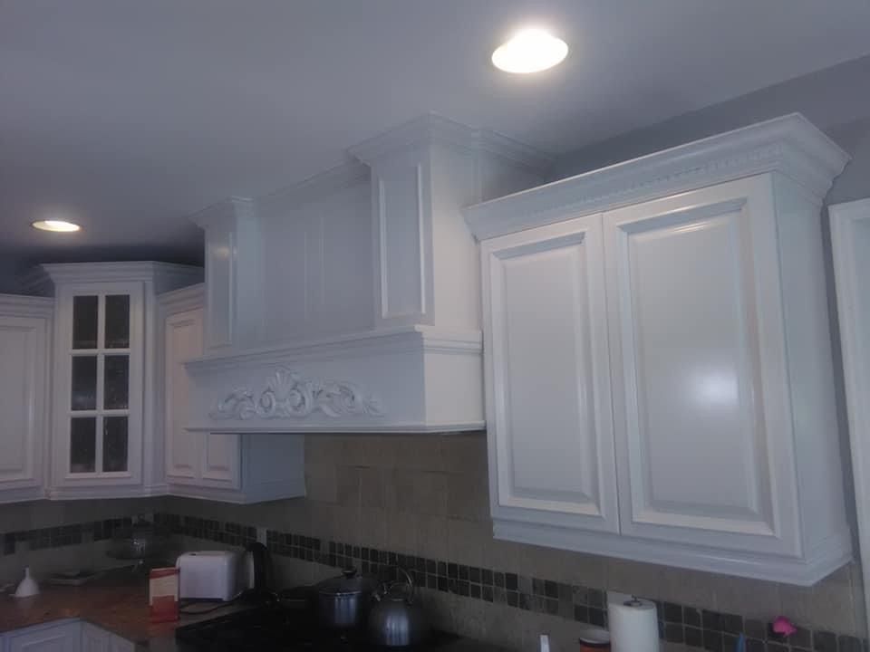 White kitchen cabinets with range hood above stove and light fixtures.