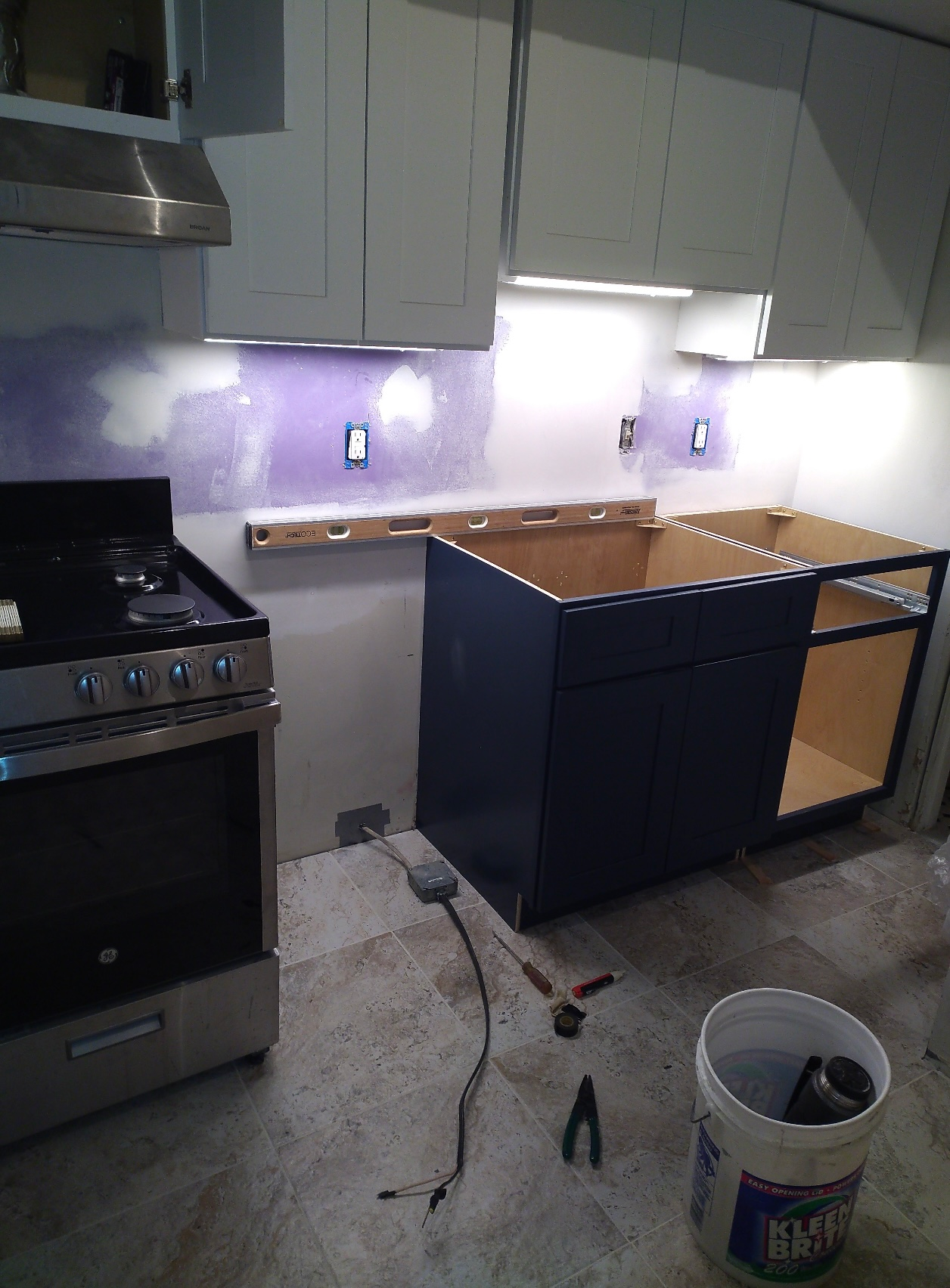 Kitchen renovation in progress: cabinets, stove, and exposed wall with purple paint visible.