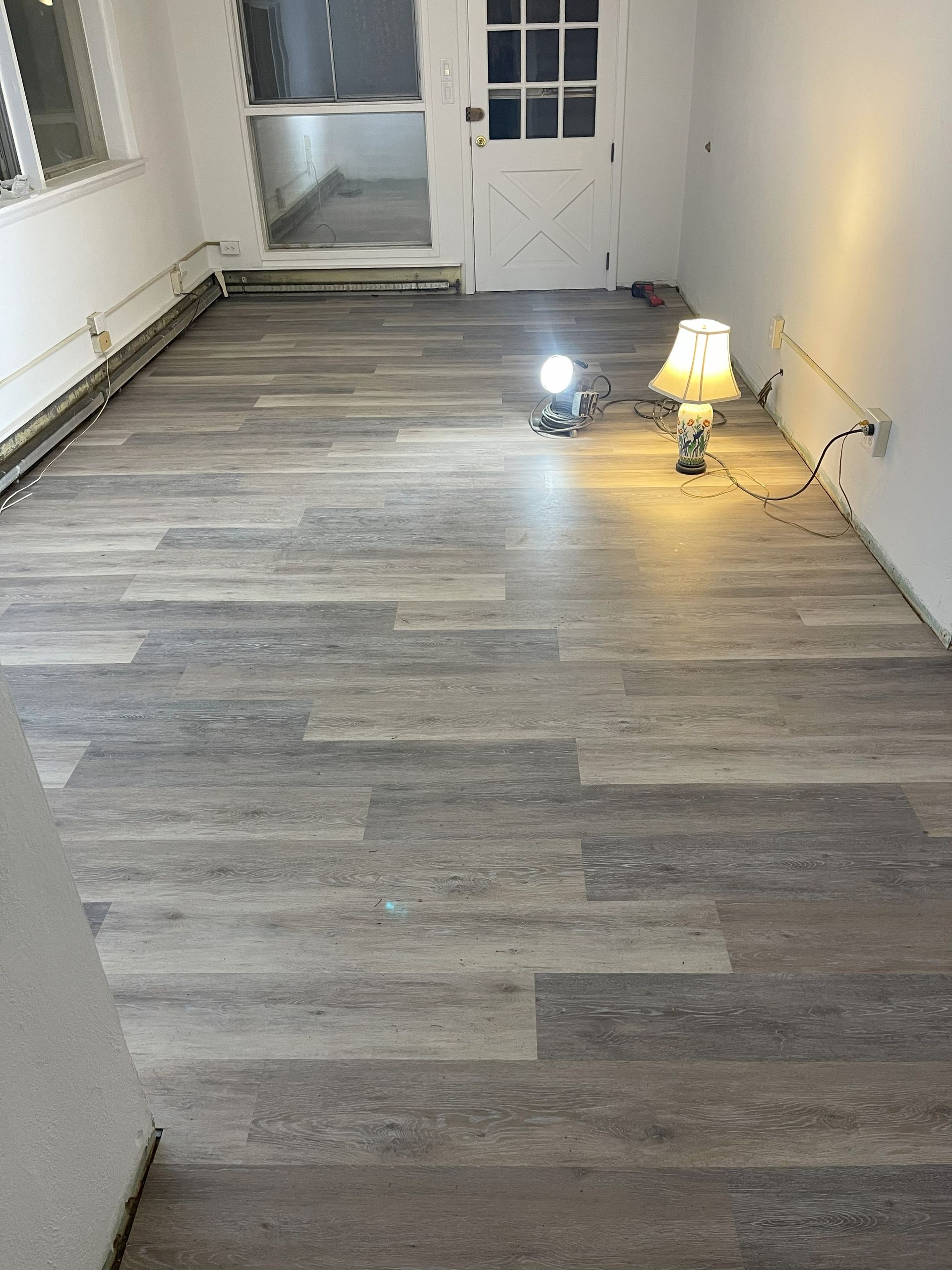 Room with wood-look flooring. White walls, door, and window. Two lamps illuminate the space.