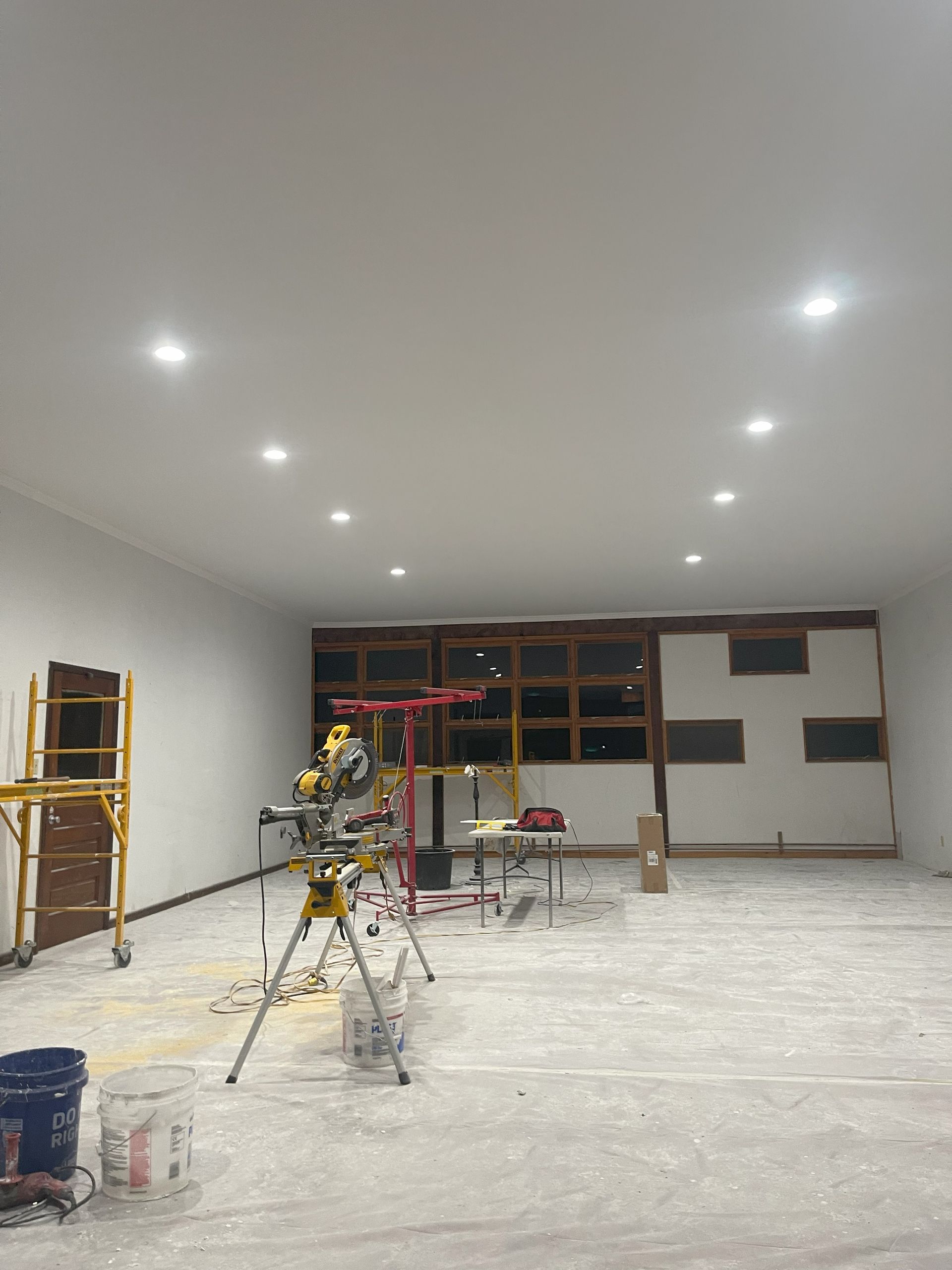 Interior of a room under construction with tools and overhead lights, unfinished walls and floor.