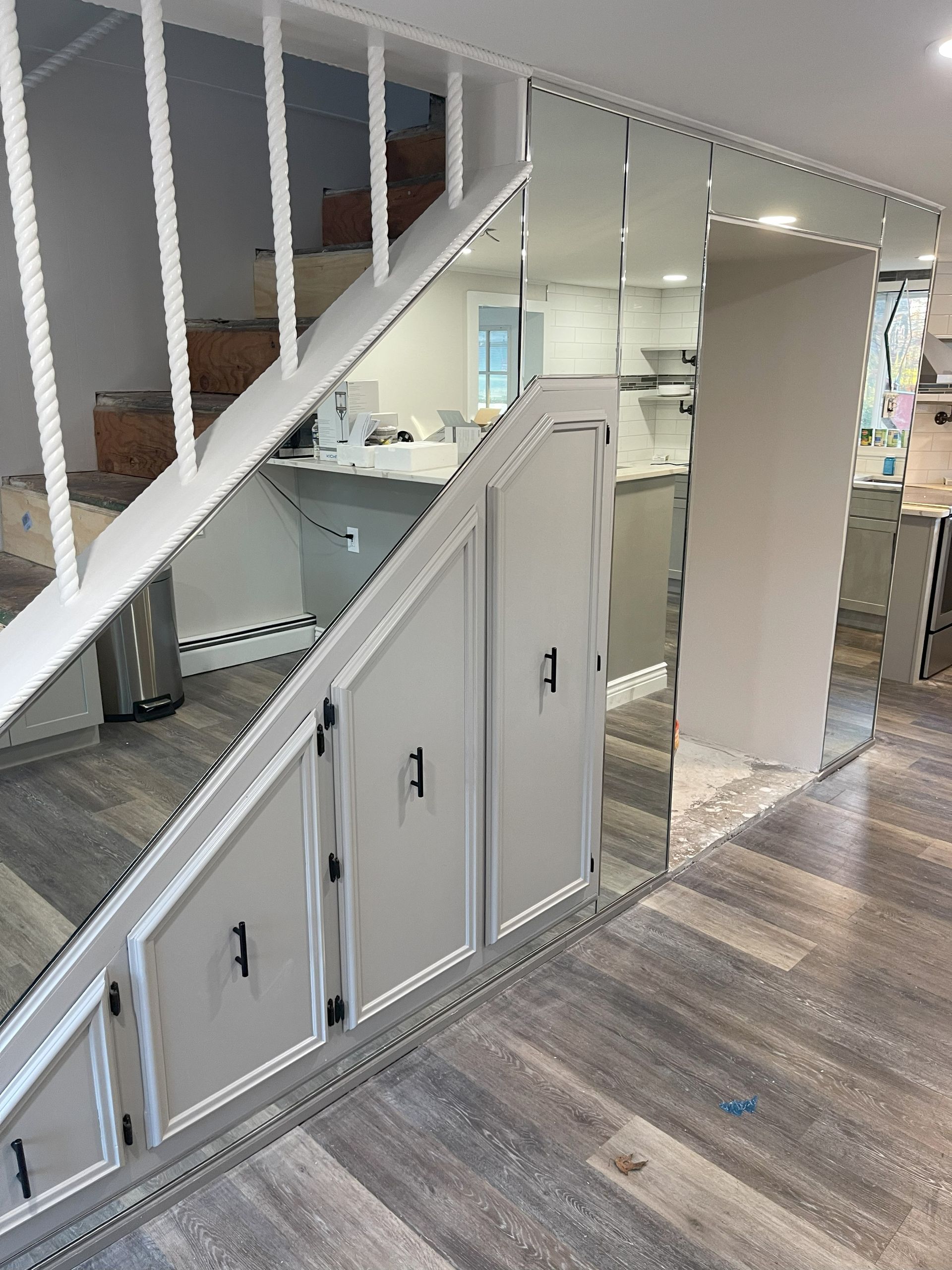 White cabinetry built under a staircase, mirrored wall, light grey flooring.