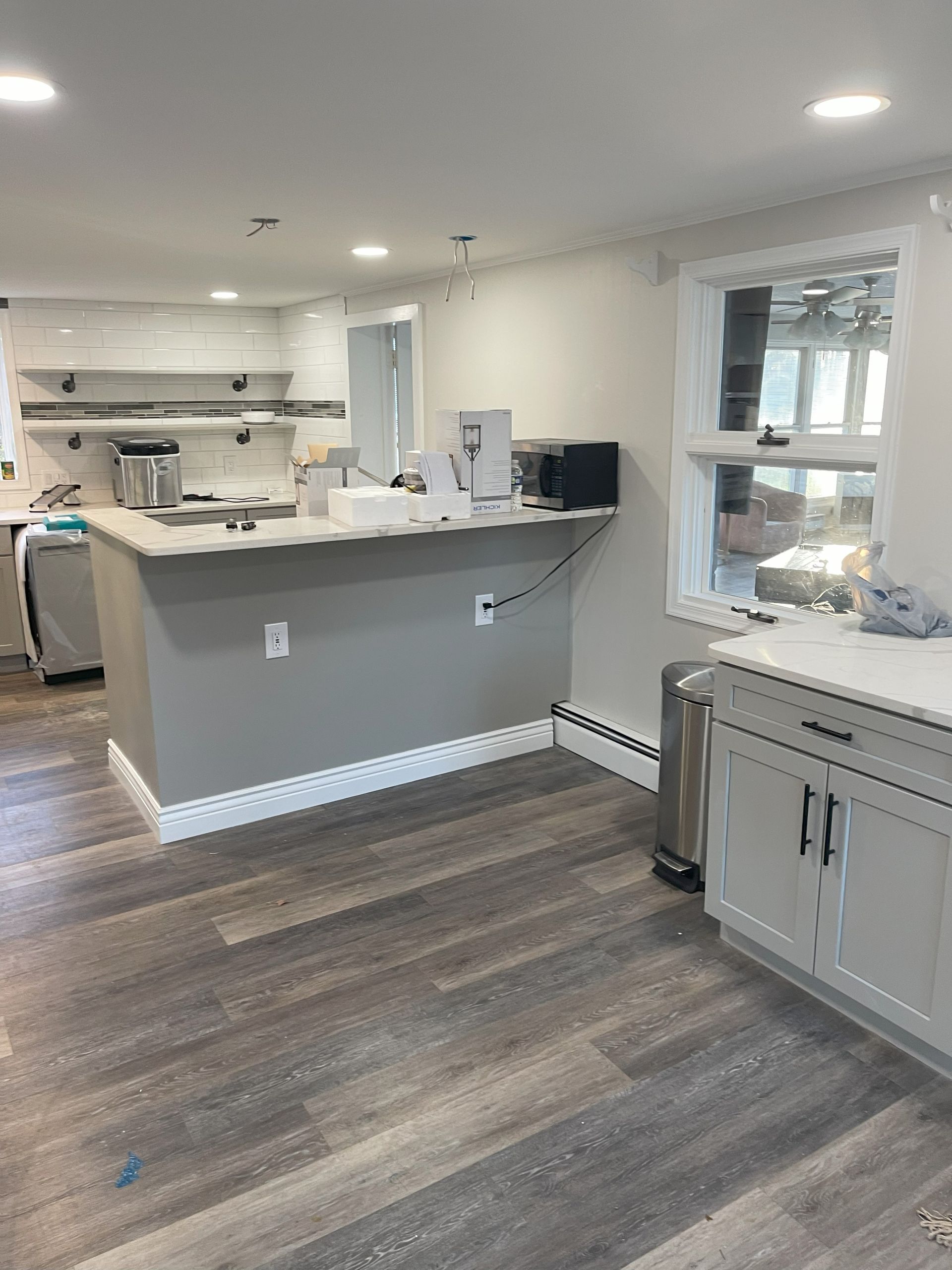 Newly renovated kitchen with gray cabinets, island, and wood-look flooring. Window on the right.