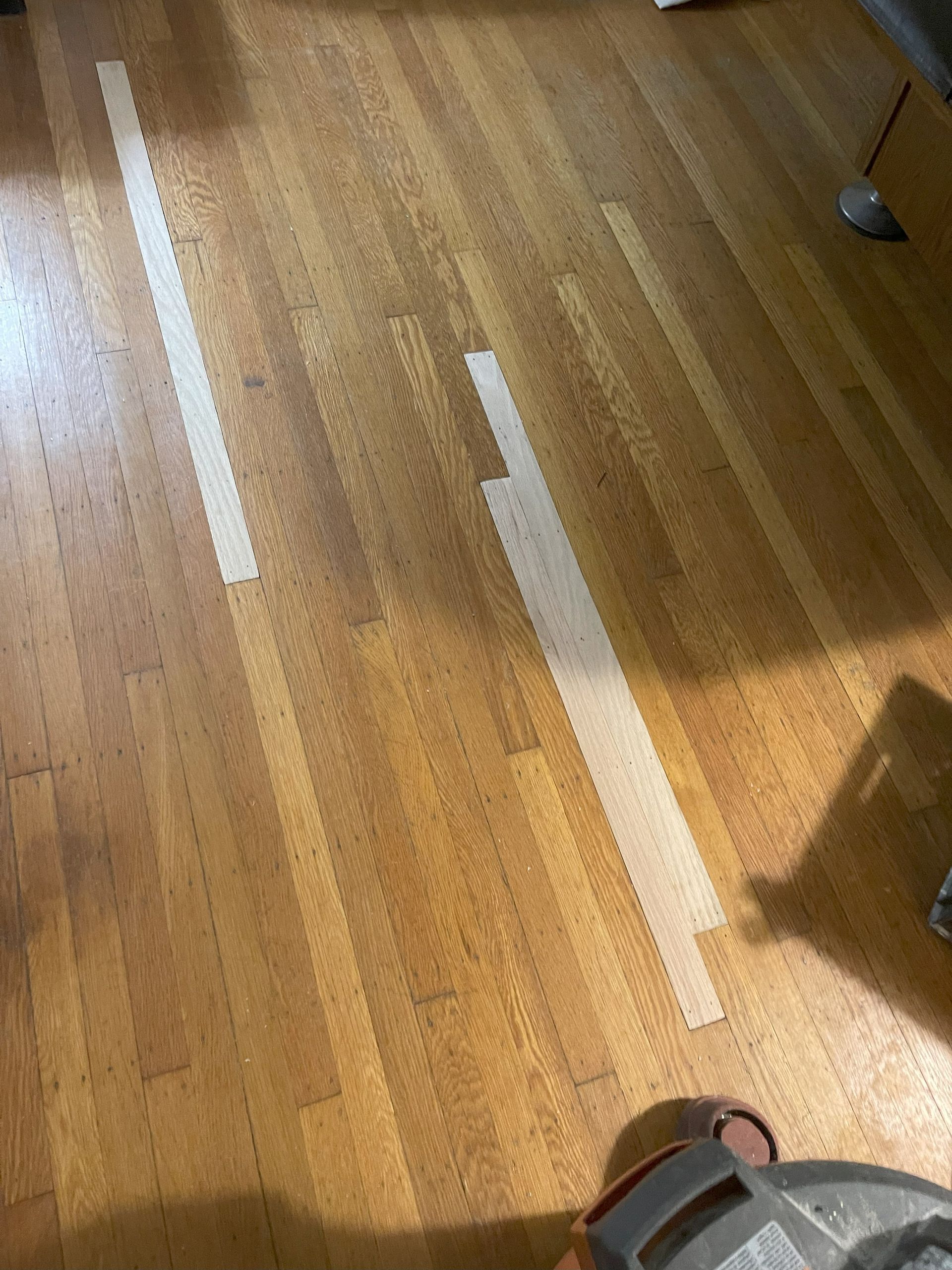 Wooden floor with light-colored strips taped down, possibly for repair or refinishing.