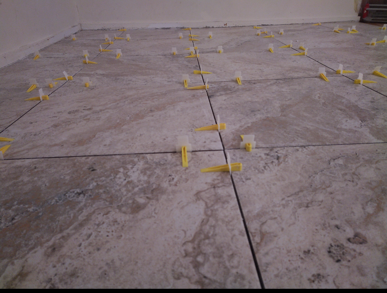 Tiles laid on a floor with yellow leveling clips in the grout lines. Beige and brown tones.