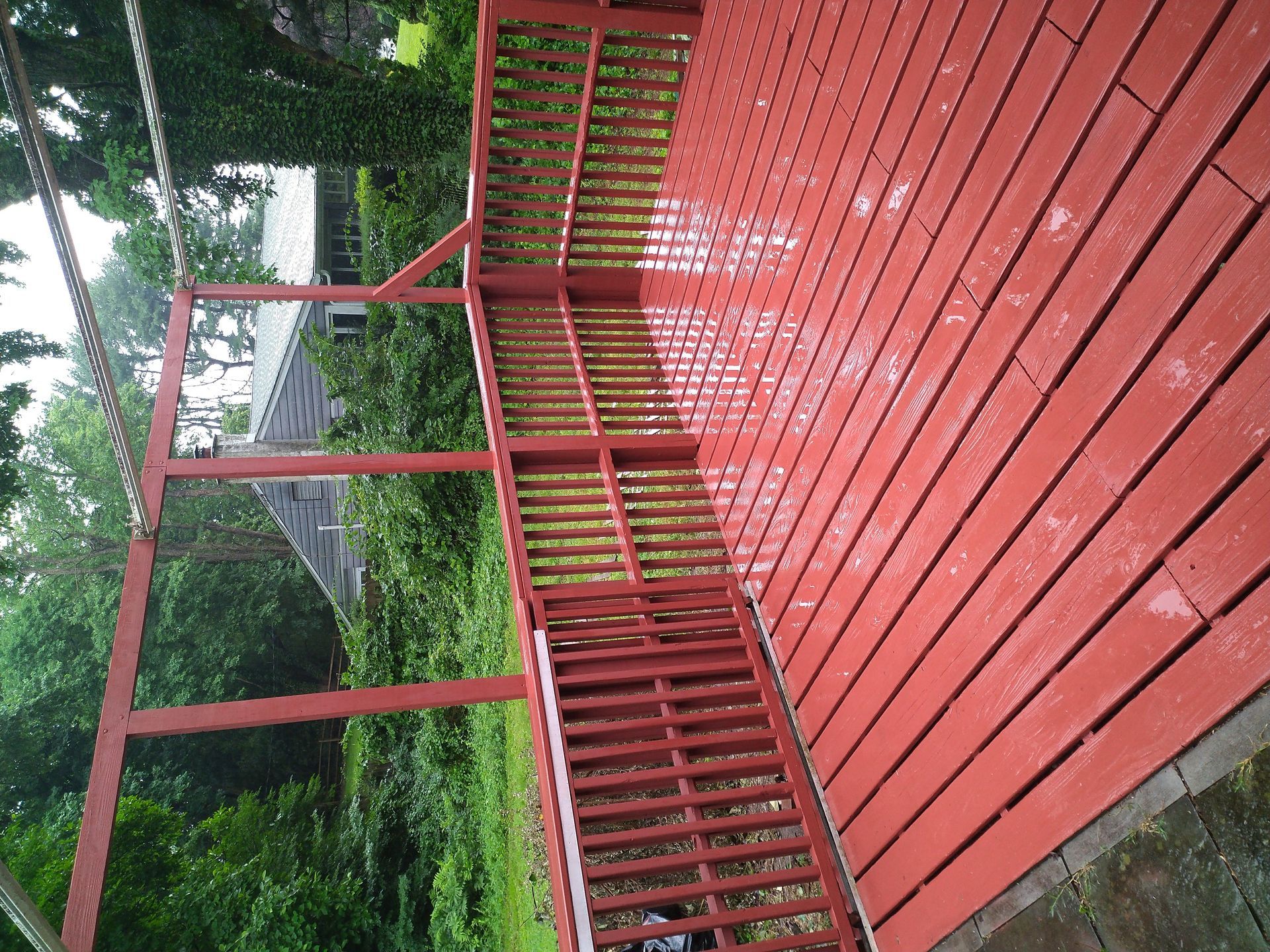 Red wooden deck with stairs leading down; green trees in the background.