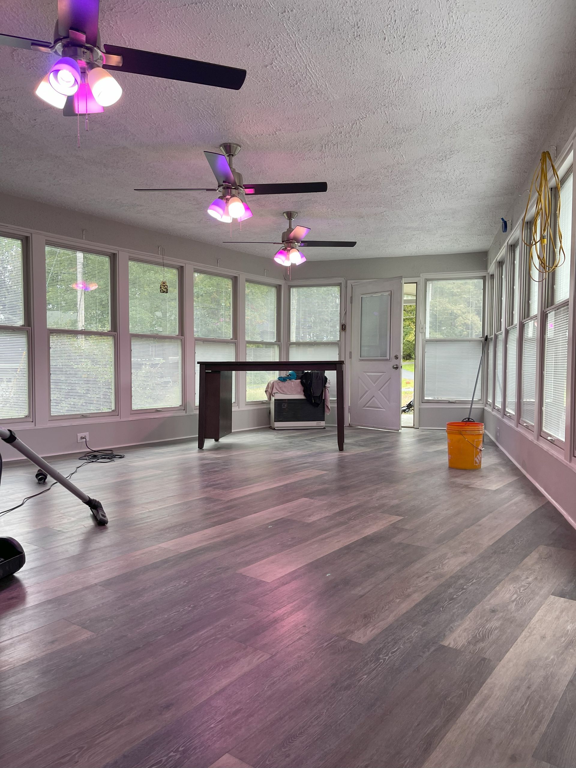 Interior of a sunroom with multiple windows, ceiling fans, and a desk. Gray floors and white walls.