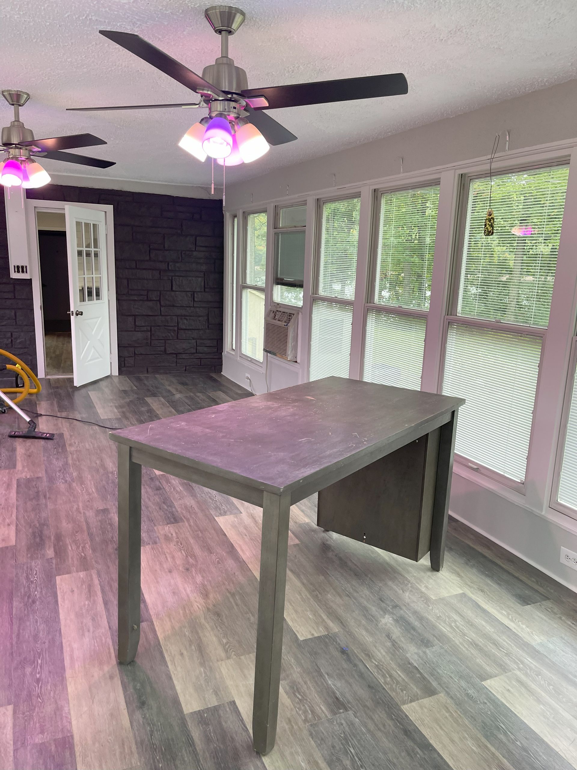 Room with grey table, windows, and ceiling fans. A door is visible in the background.