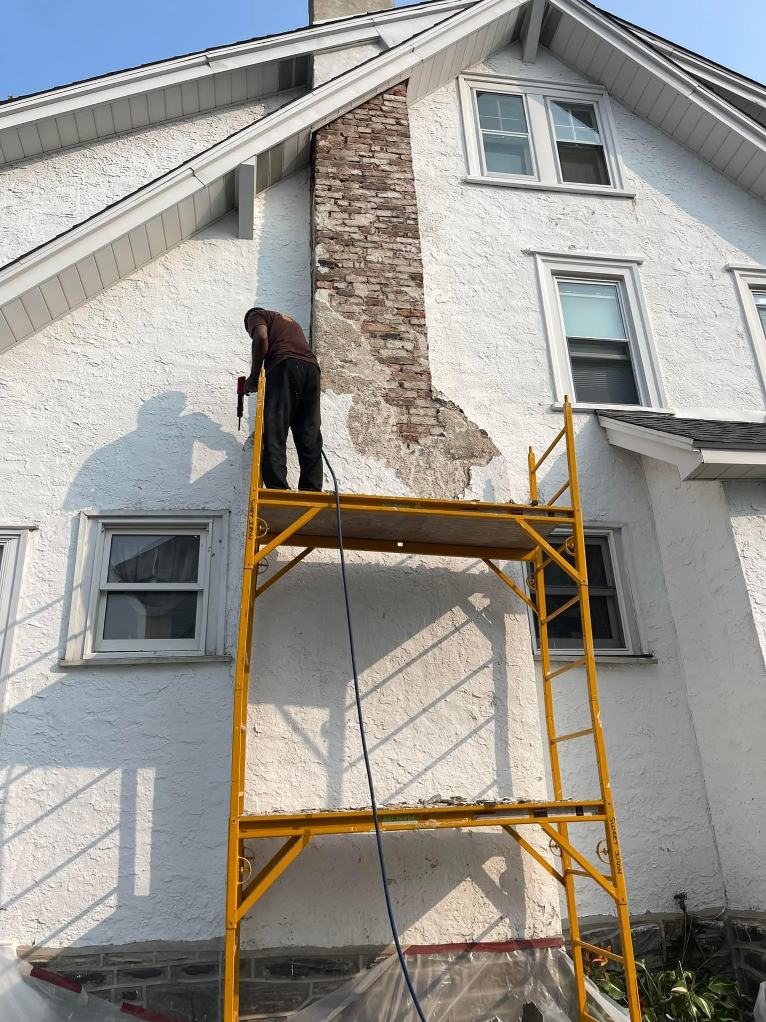 Man on scaffolding repairing chimney on a white house.