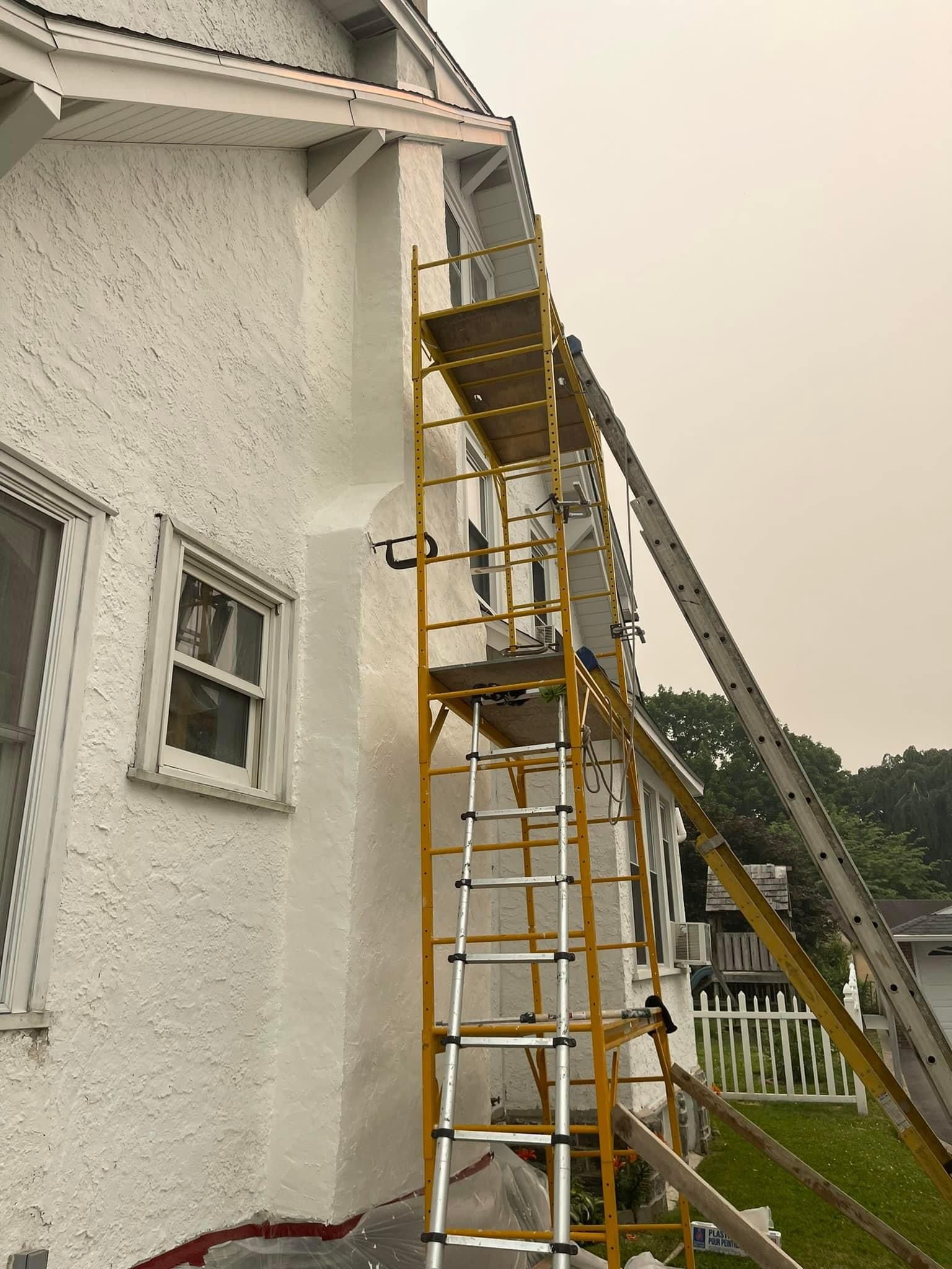 Scaffolding and ladder leaning against white stucco house, overcast sky.