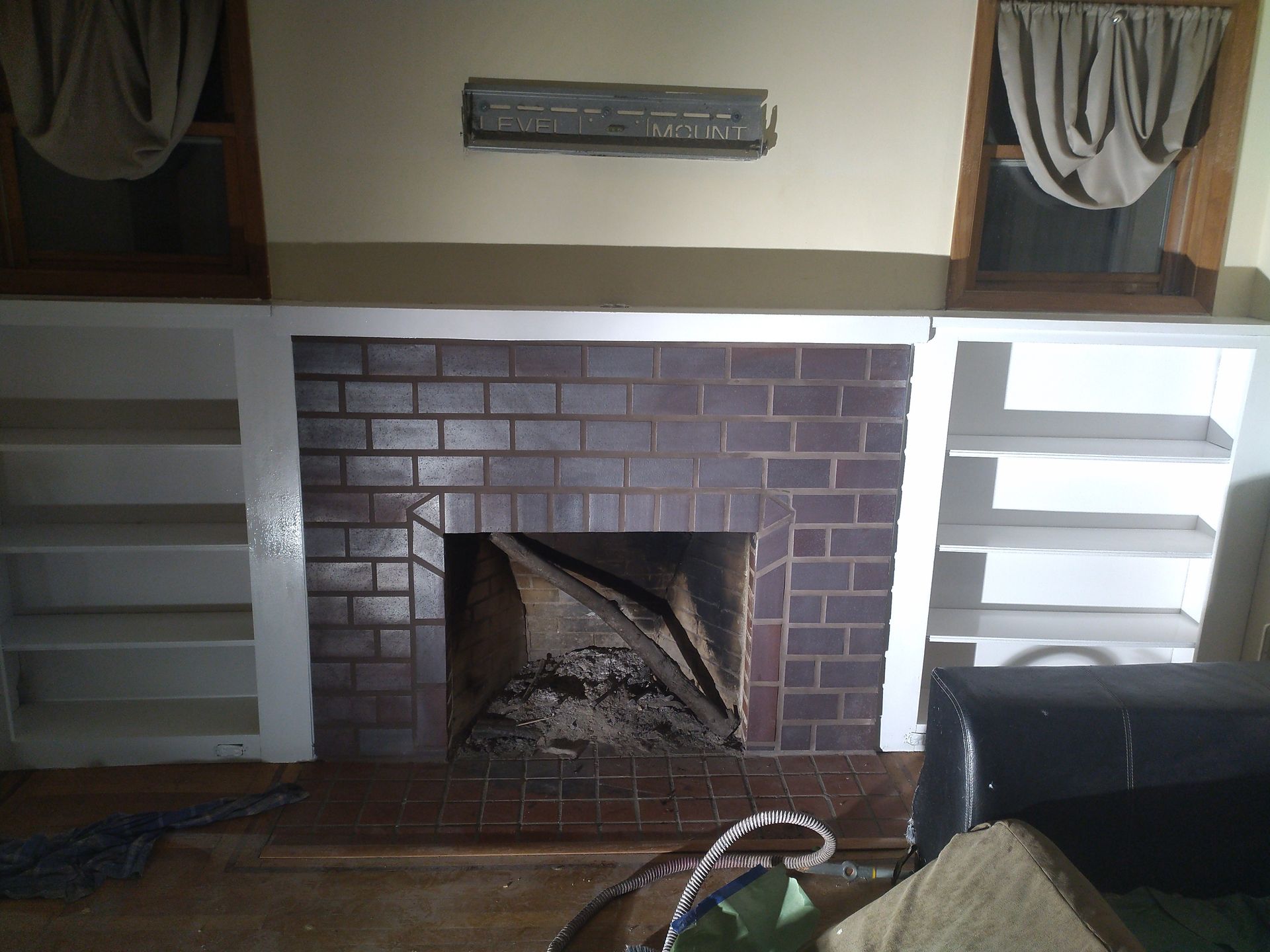 Brick fireplace with built-in white shelves and two windows with curtains on each side.