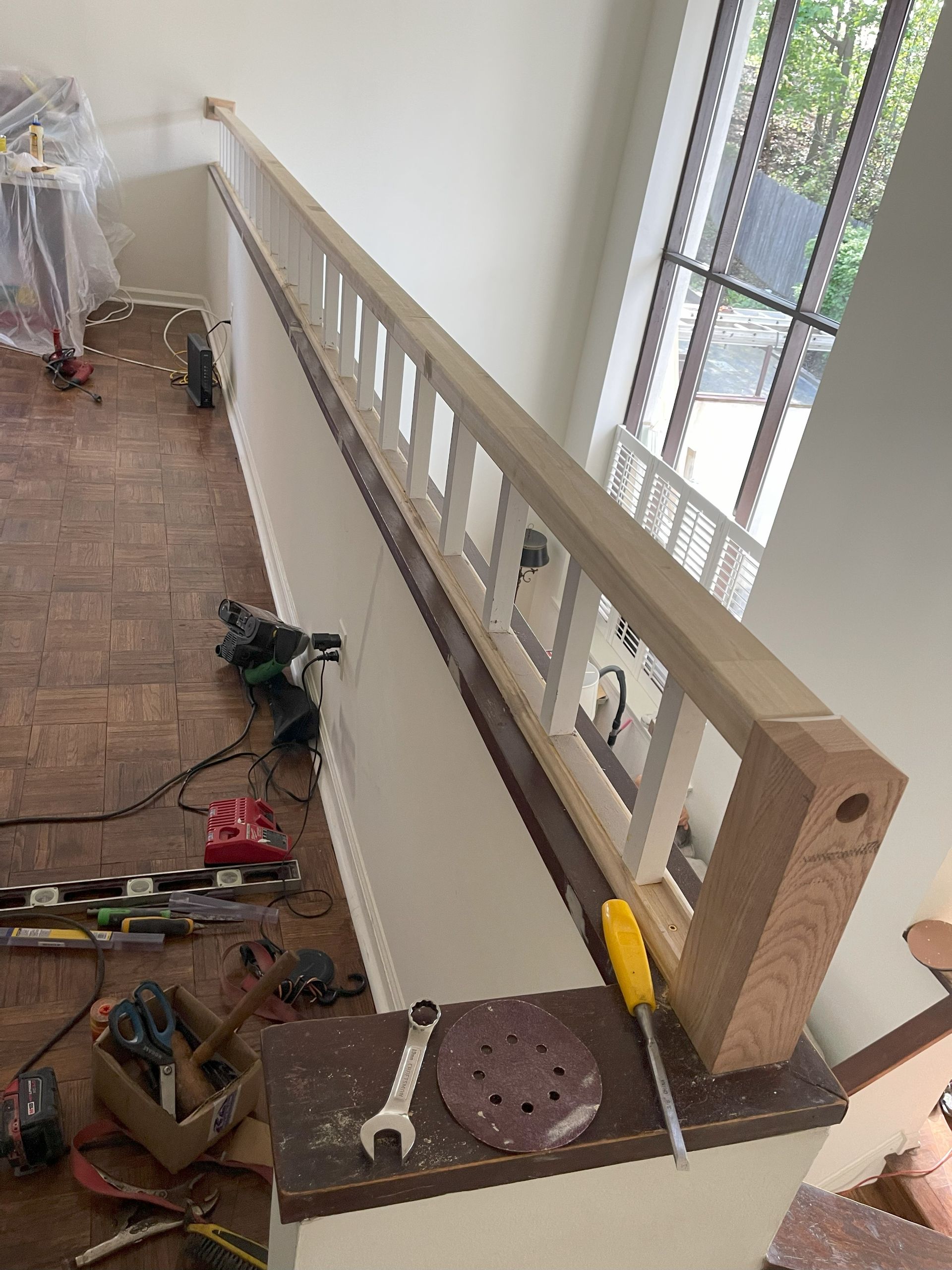 Interior view of a staircase railing being constructed; wood and white elements, tools on a ledge below.