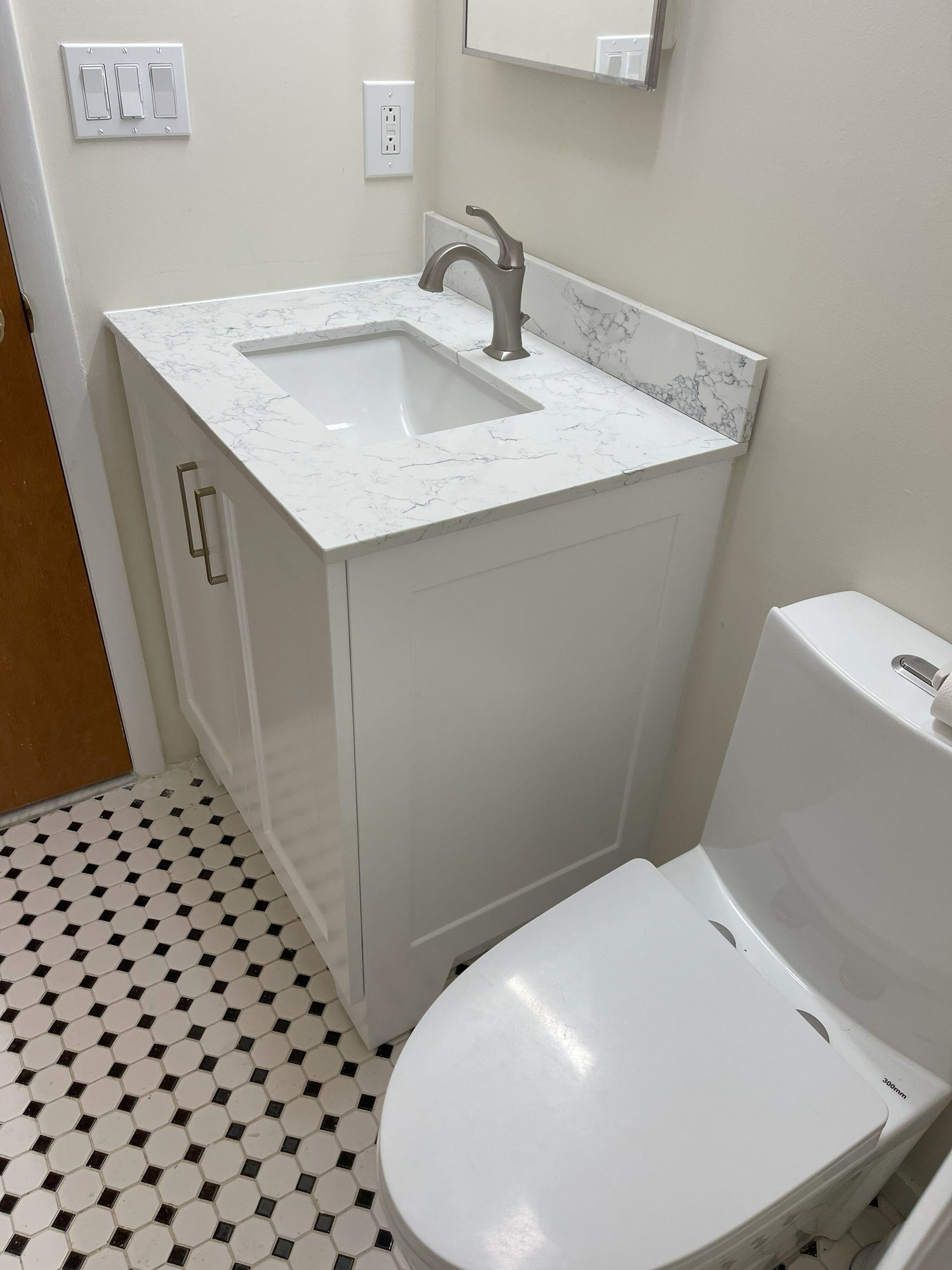 White bathroom vanity with sink and faucet, next to a white toilet; black and white tiled floor.