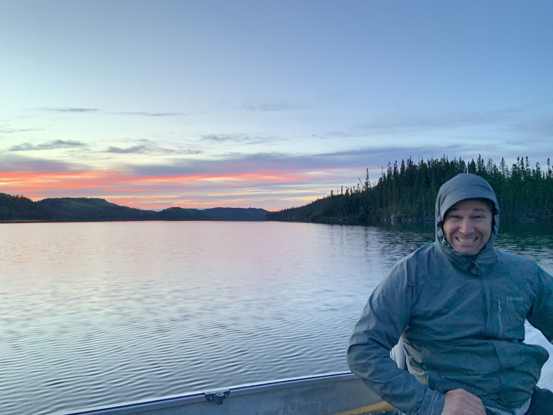 Un homme est assis dans un bateau sur un lac au coucher du soleil.