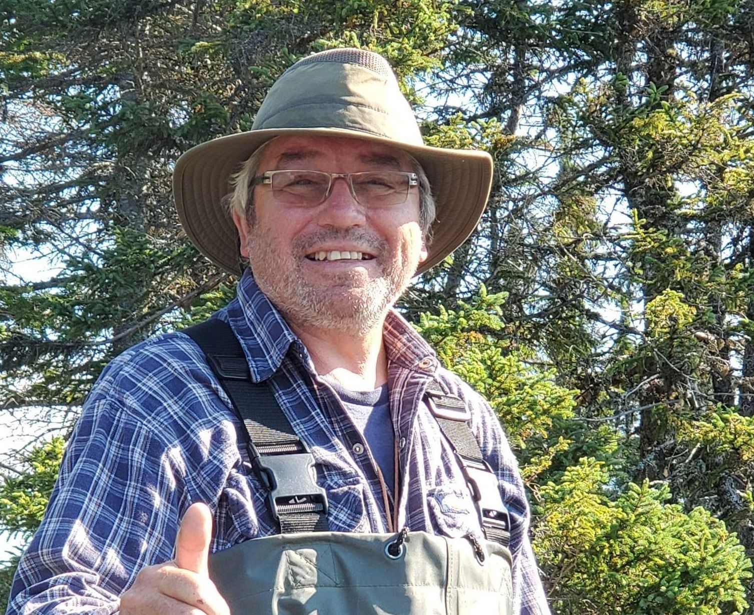 A man wearing a hat and waders is giving a thumbs up