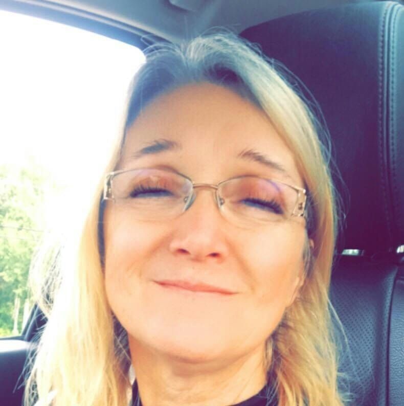 A woman wearing glasses is smiling while sitting in a car
