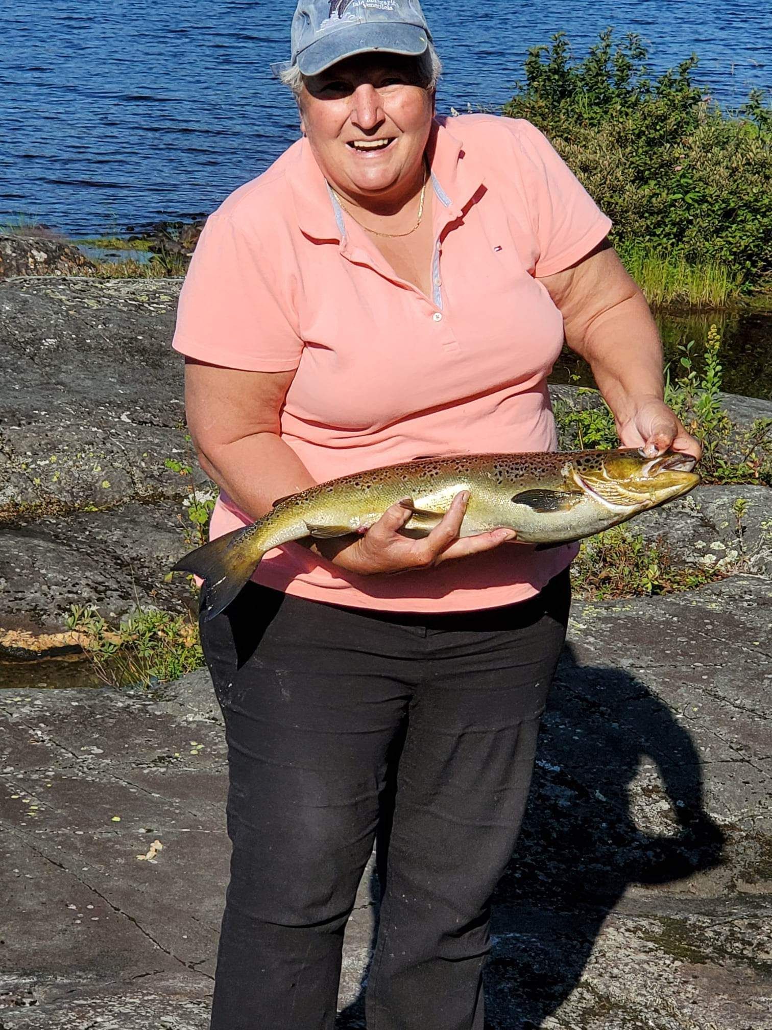 Une femme en chemise rose tient un gros poisson dans ses mains.