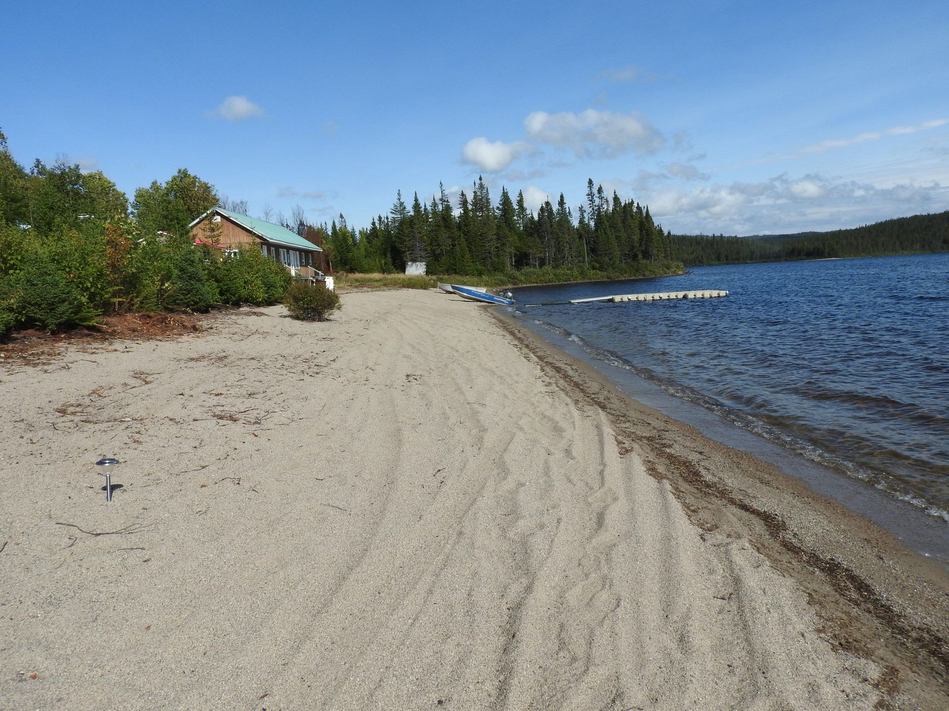 Une plage de sable à côté d'un lac avec une maison en arrière-plan