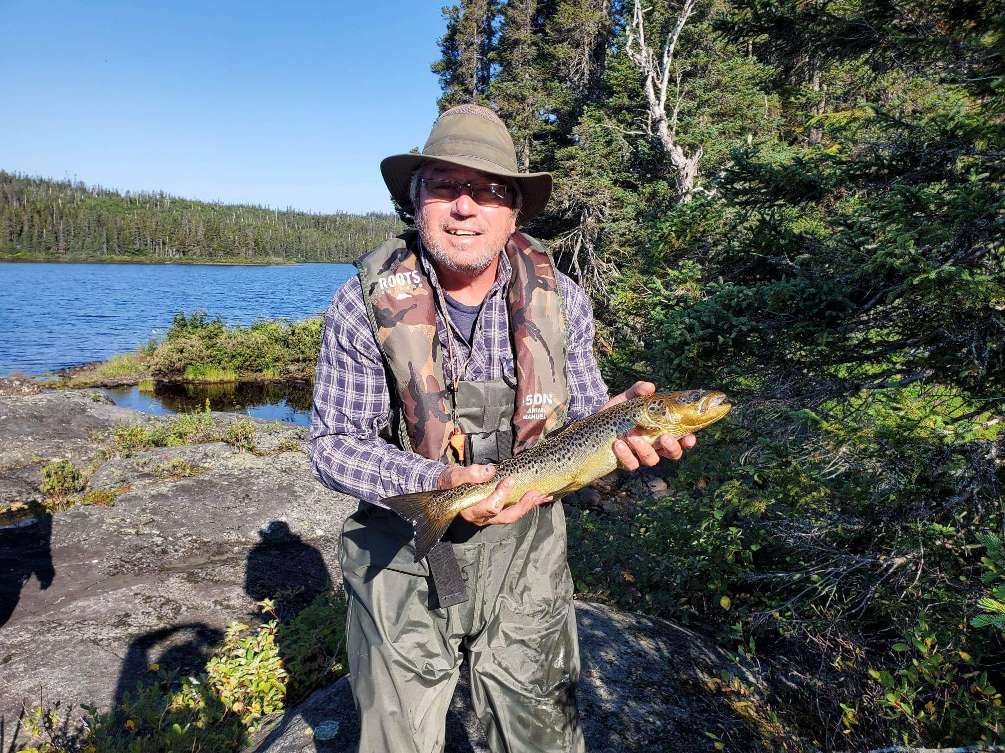 Un homme tient un gros poisson dans ses mains devant un lac.
