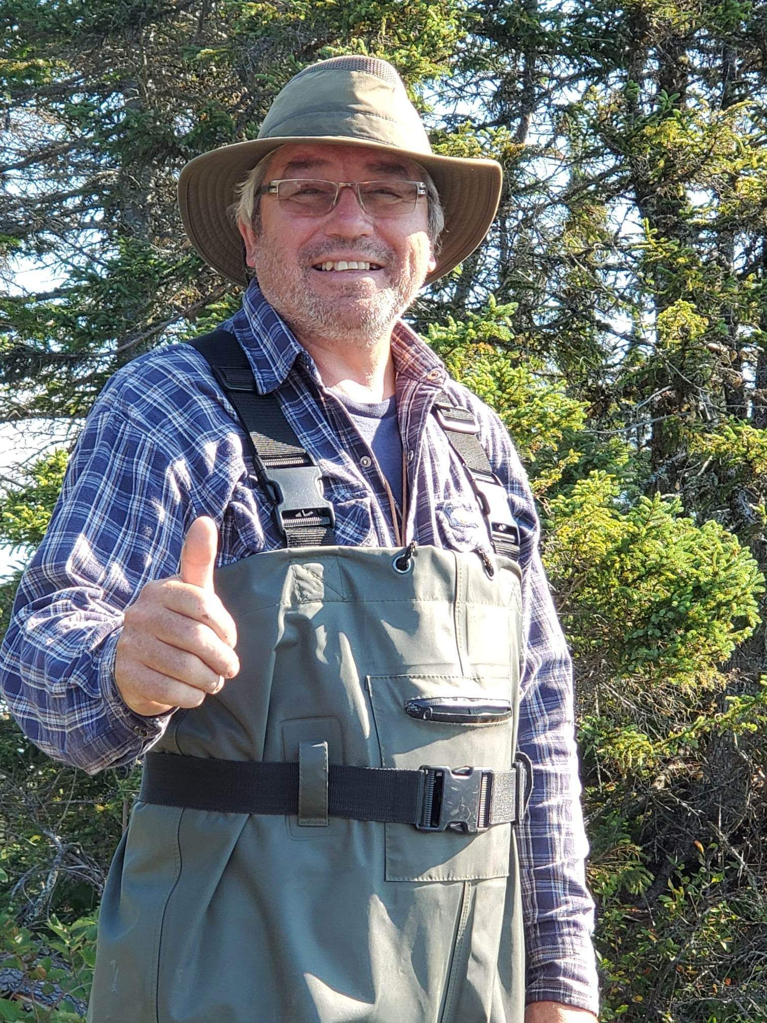 Un homme portant un chapeau et des cuissardes lève le pouce.