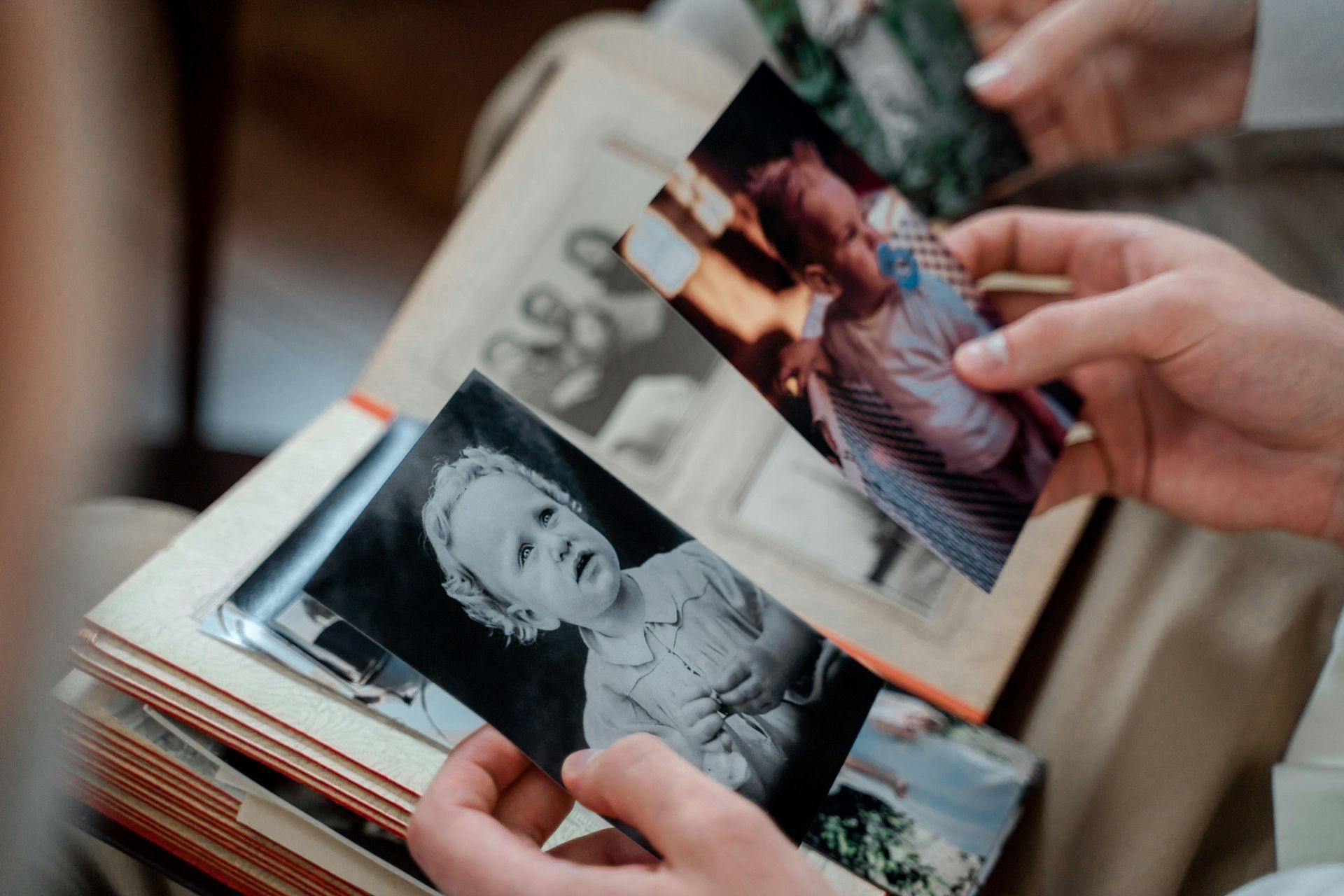 Hands holding and looking at photos in an album, including a black and white baby portrait.