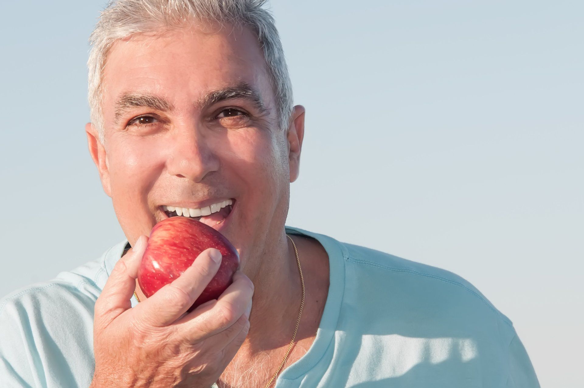 Prosthodontics - a man is smiling while eating an apple .