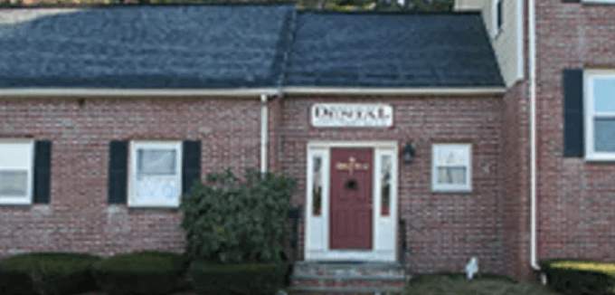 North Acton Dental is located in a brick house-style building  with a red door and a sign that says North Acton Dental