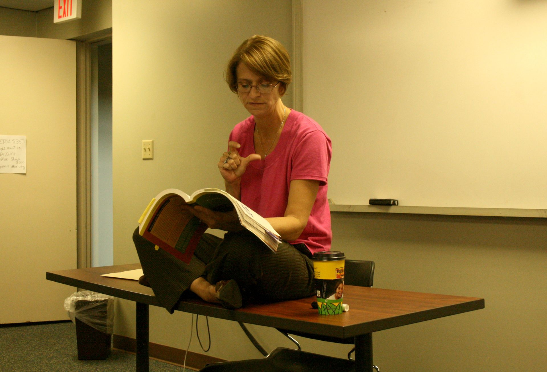 Dr. Christine Marley-Frederick reading with legs crossed on a classroom table.
