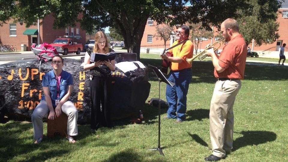 Miller playing acoustic guitar with a music group performing outside on Union's campus, in front of Spirit Rock.