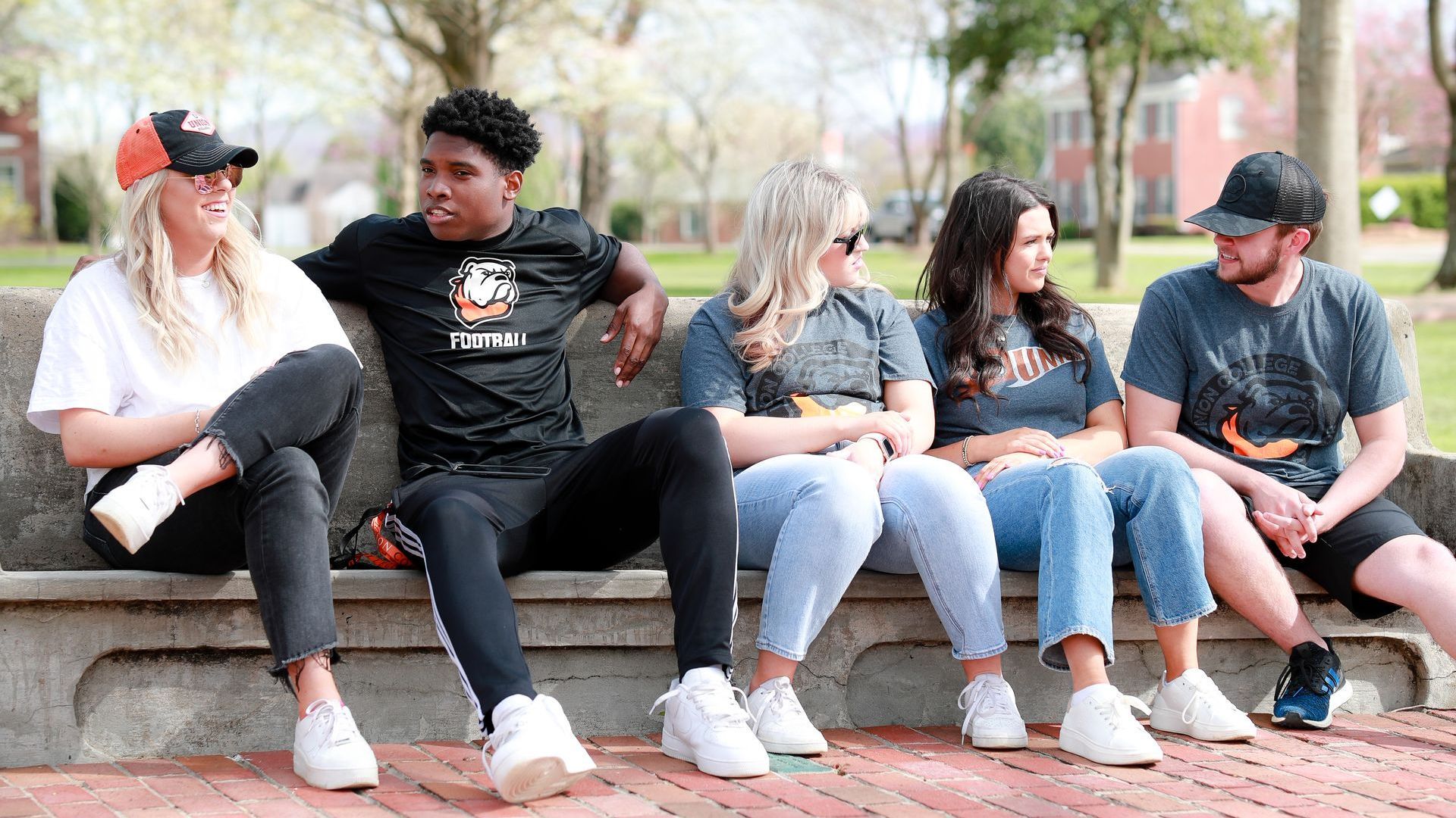 students sitting on a bench talking on the front walkway of campus