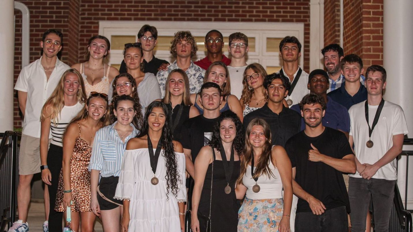 A group of twenty men and women in casual and formal attire stand together in front of a brick building with white pillars on a set of stairs. Several are wearing their Circles medallions. One male student is giving a thumbs up.