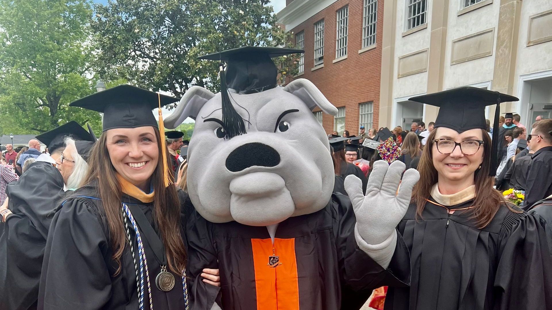 Lynn and Amanda with Union's mascot, Mack the Bulldog, all wearing caps and gowns on Union's campus.