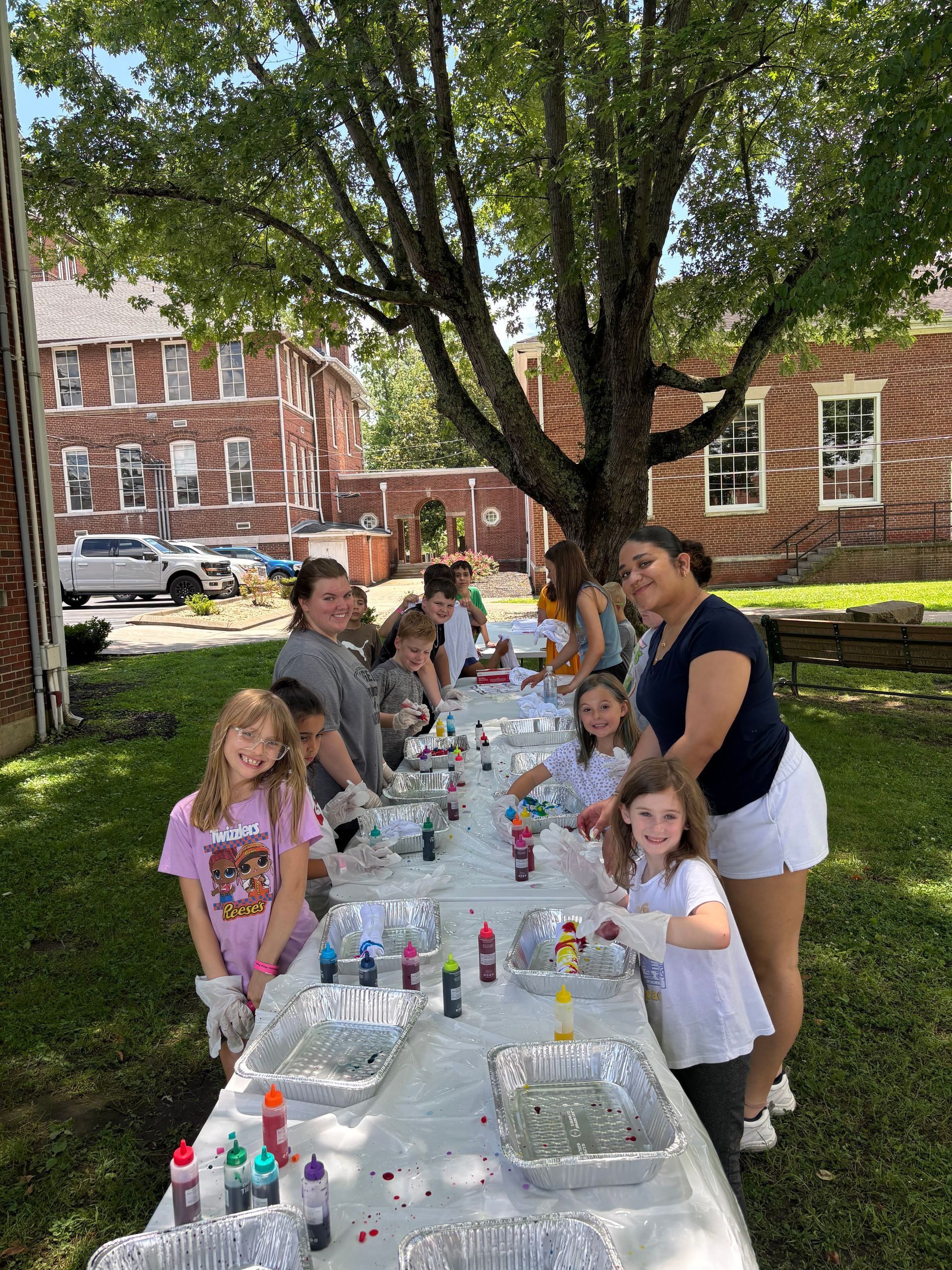 Club kids and young adult staff members tie-dye t-shirts on the lawn beside Norton Hall.
