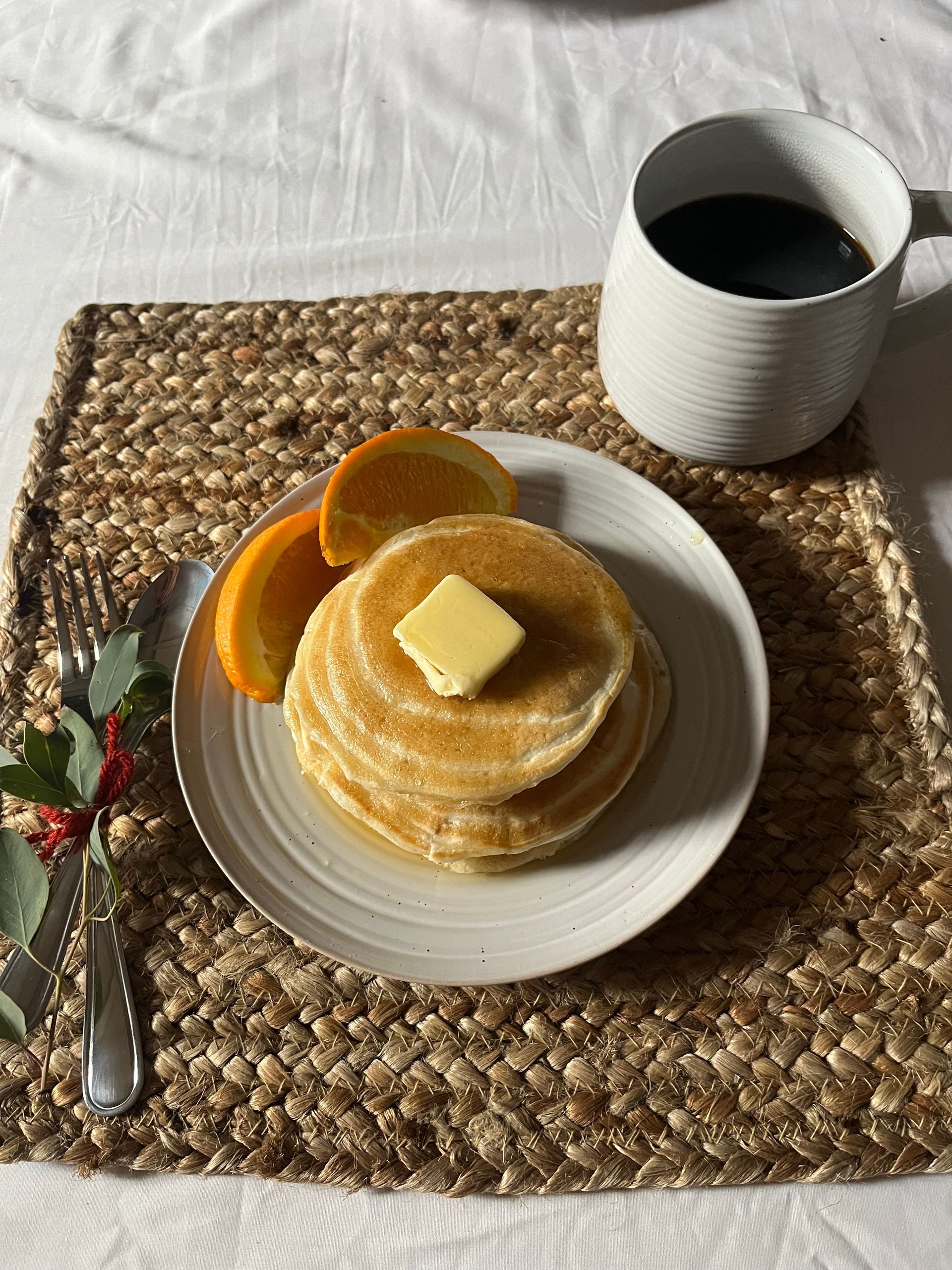 A plate of pancakes and oranges sits on a woven tray with a fork and a coffee cup.