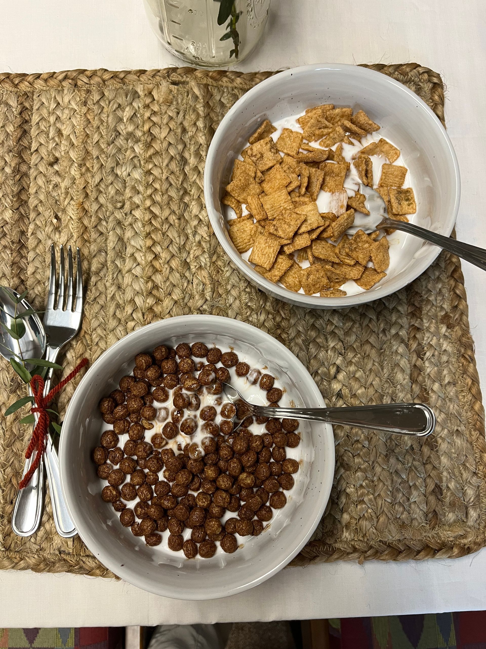 Two bowls of cereal made with glue and a set of utensils sit on a woven tray.