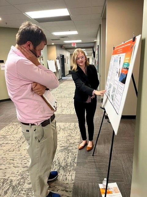 Amelia pints out a section of her reserach poster to an onlooker