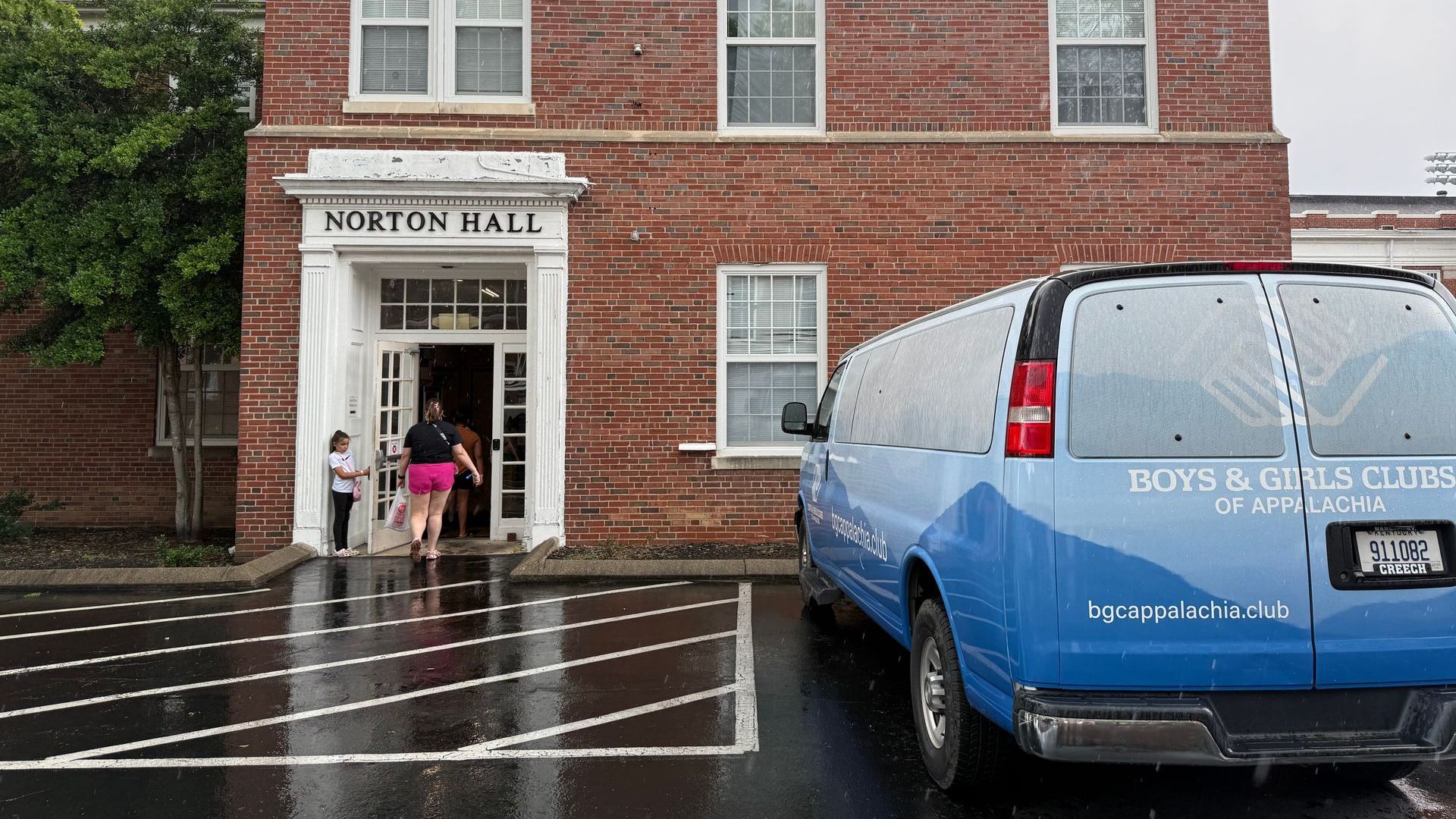 Children enter Norton Hall, a brick building with a Boys & Girls Club van parked out front.