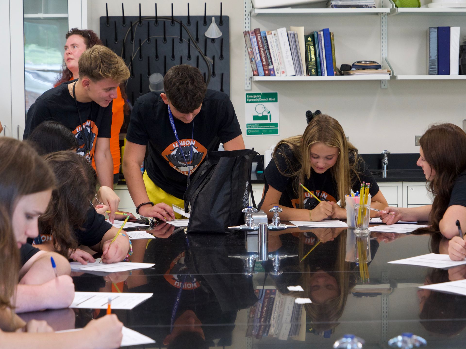 Students sitting at a black table and filling out papers with professor Libby Megna in the background.