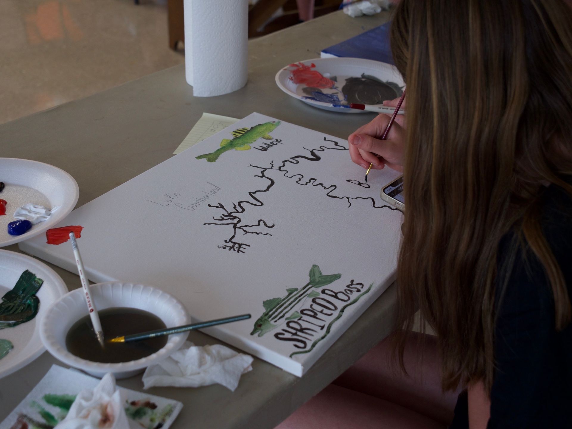 A student painting a striped bass onto a canvas.