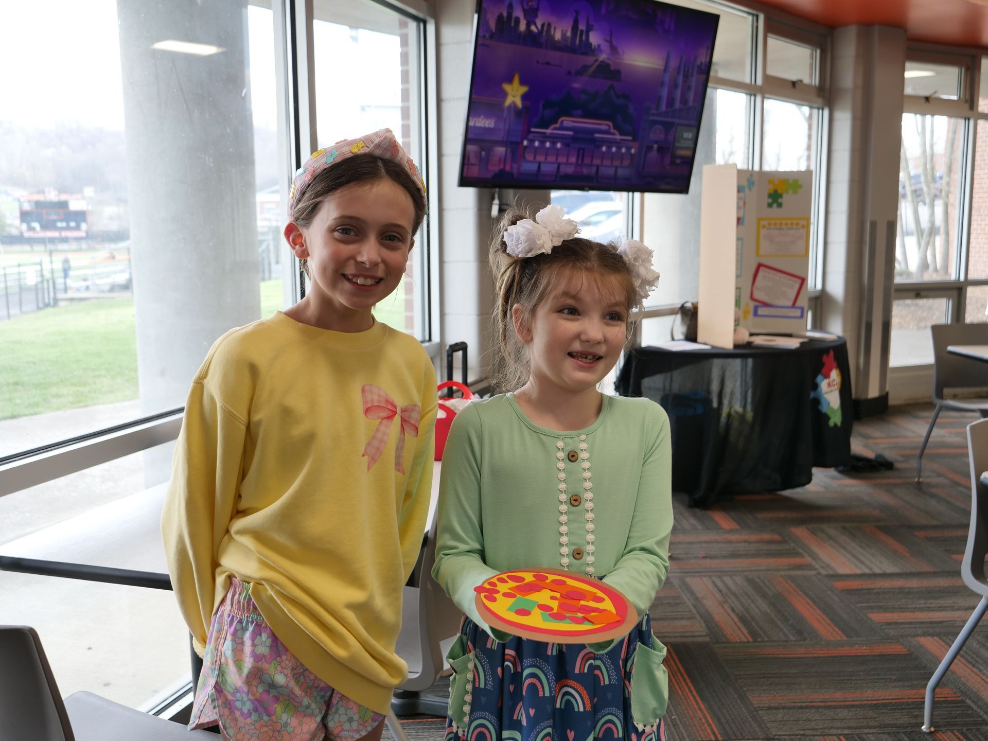 Two kids smiling and holding a decorated paper pizza.