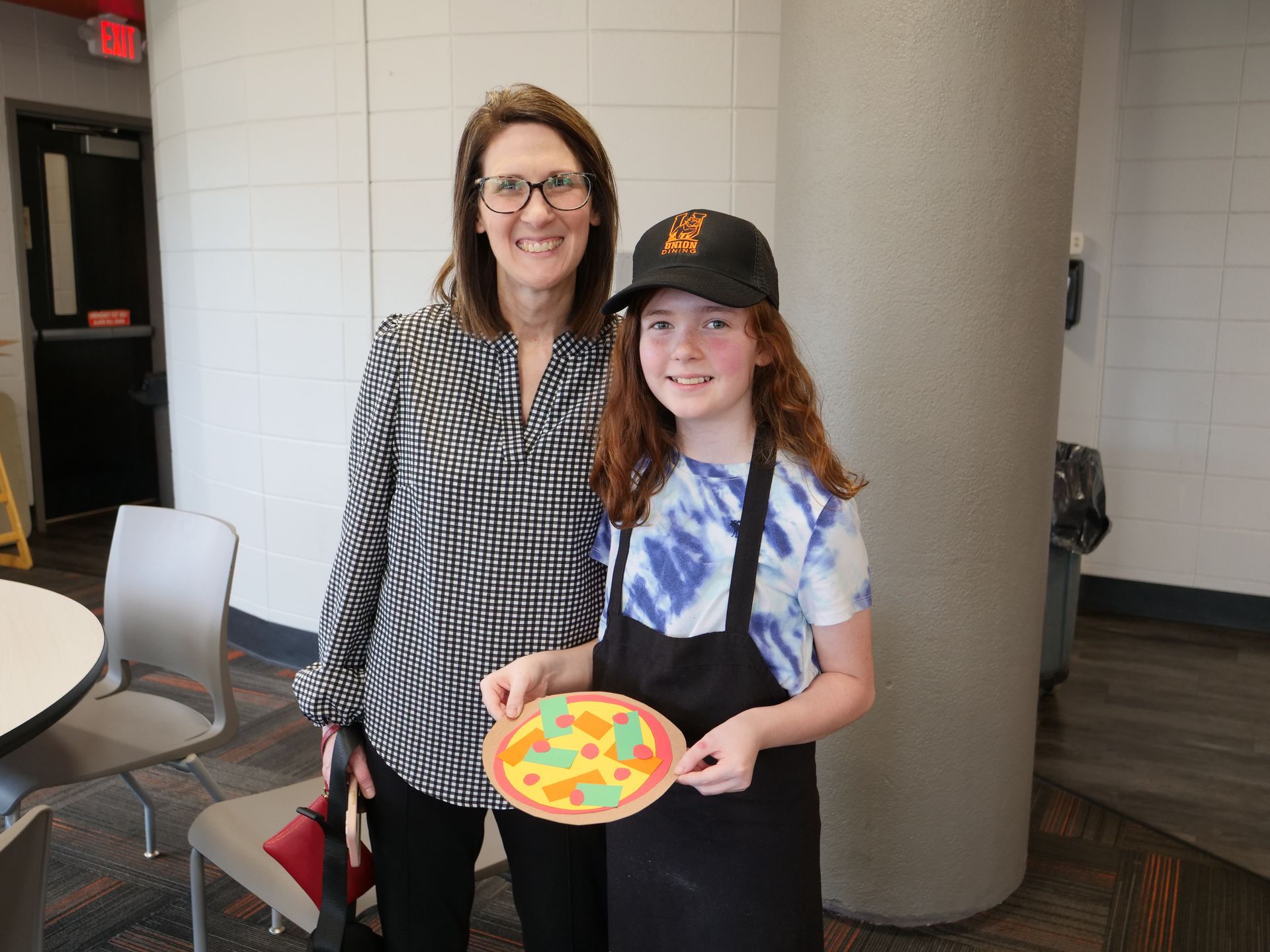 A child attendee and a parent smile holding a decorated paper pizza.