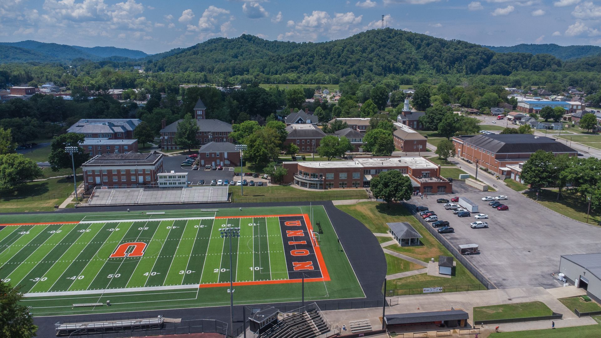 aerial drone photo of campus overlooking football field with mountains in the background