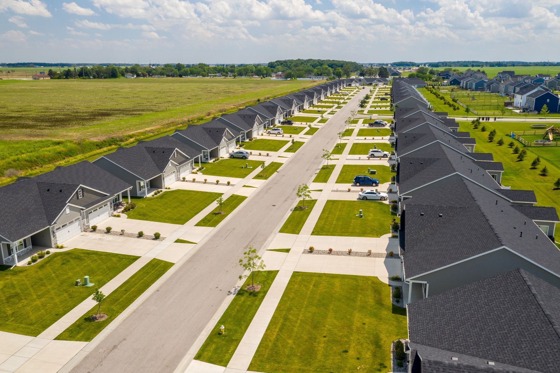 Aerial view of a suburban neighborhood with rows of houses, green lawns, and a paved street.