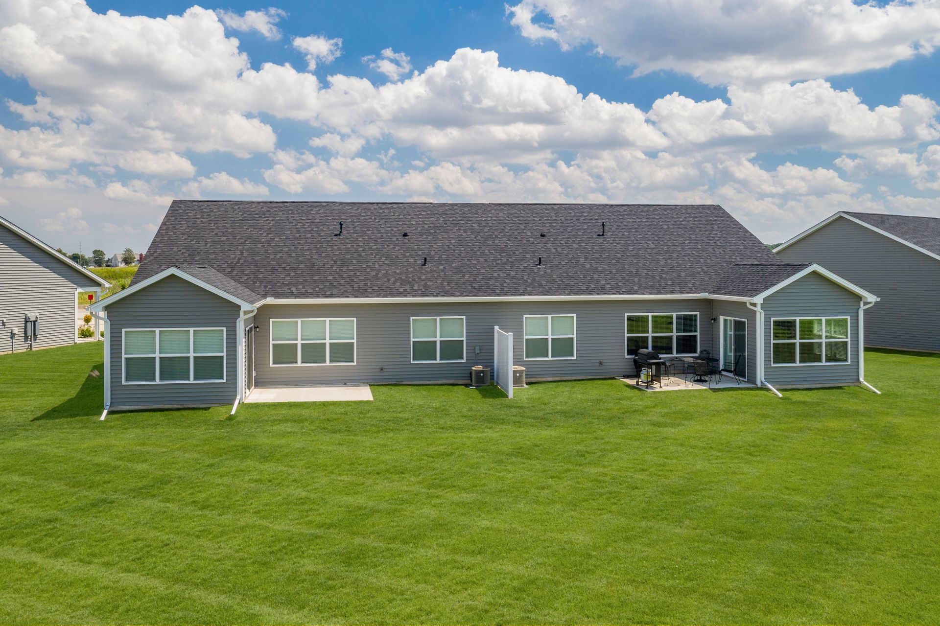Rear view of a gray house with multiple windows and a green lawn under a partly cloudy sky.