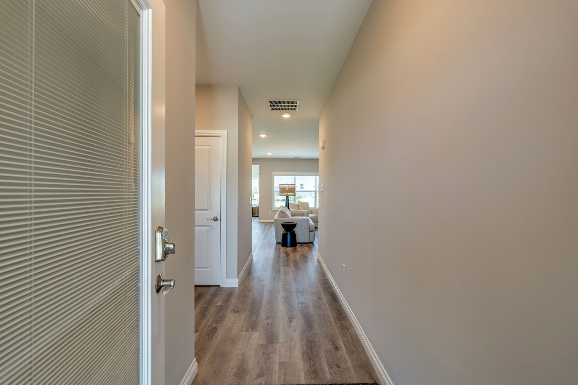 Entryway with open front door, leading to a hallway with a light wood floor, and to a living room.