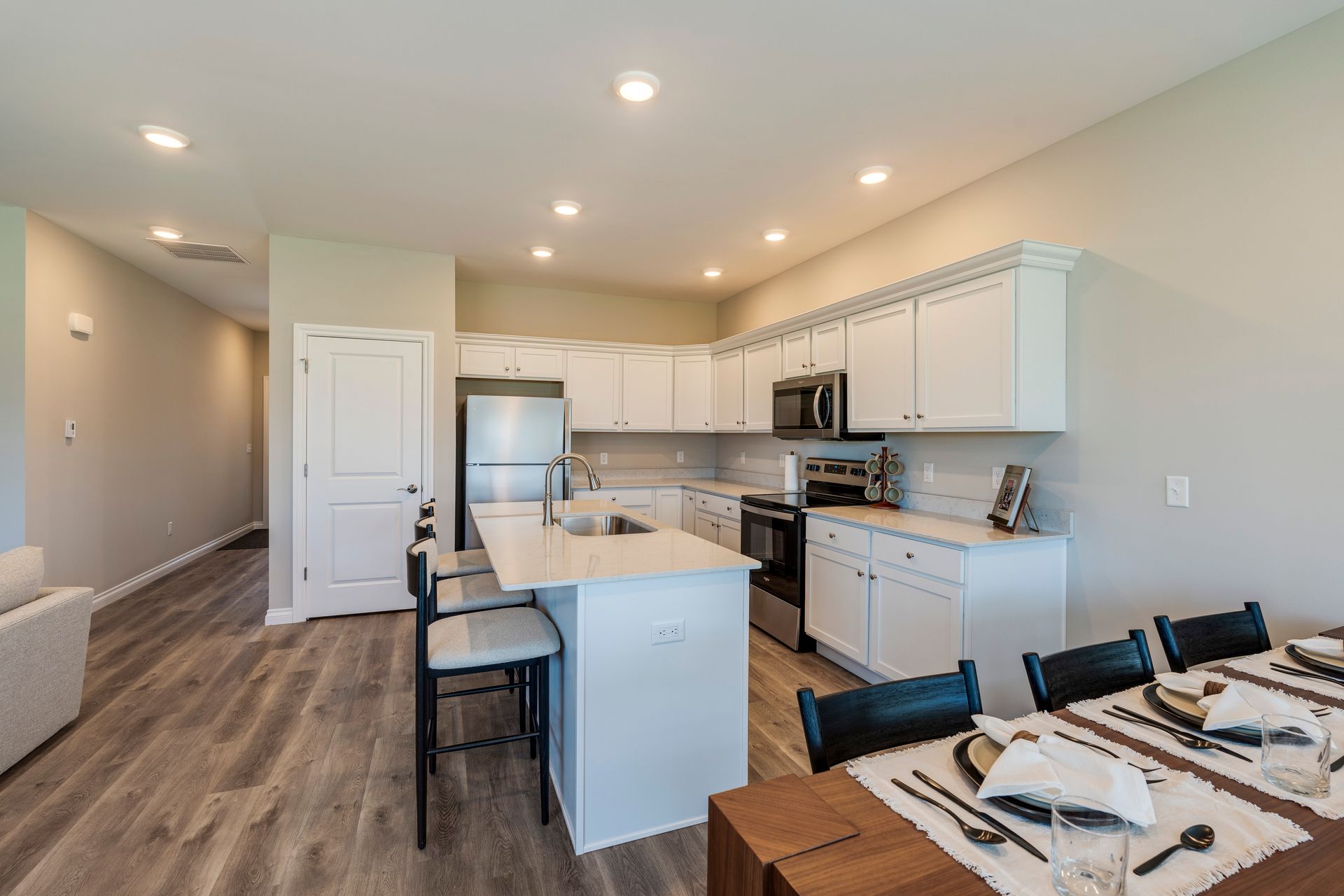 Kitchen with white cabinets, stainless steel appliances, island with bar stools, and dining table.