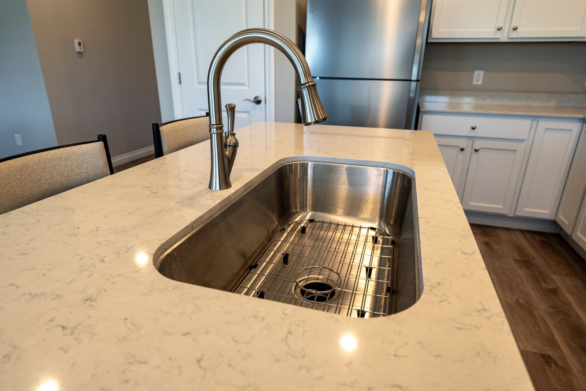 Stainless steel kitchen sink in a light-colored countertop, with a pull-down faucet, in a modern kitchen.